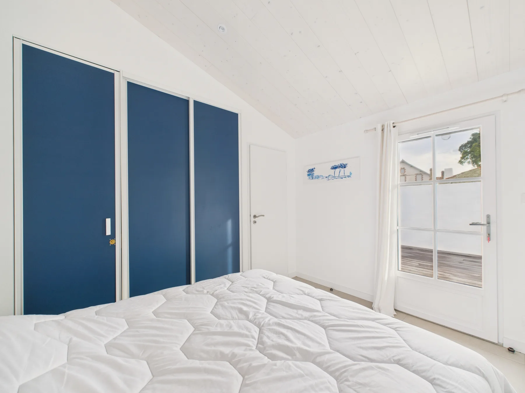 A bright bedroom with a bed and blue wardrobe doors.