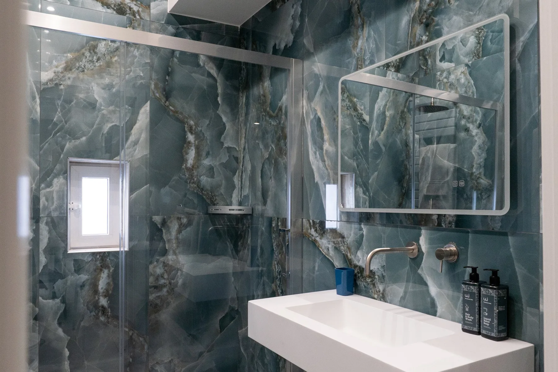 Un lavabo de baño con un lavamanos blanco y espejos grandes sobre paredes oscuras estampadas.