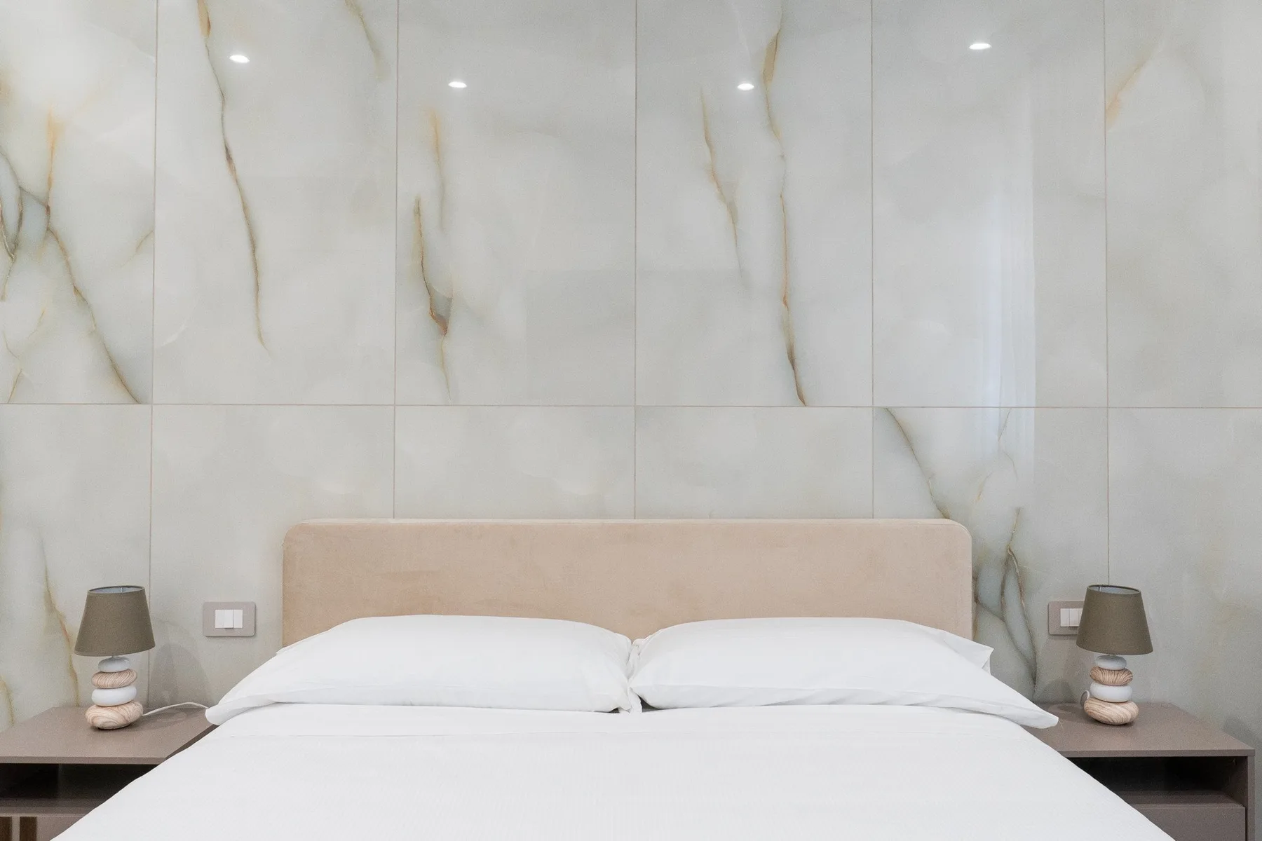 A bedroom with a bed against a marble-patterned wall.