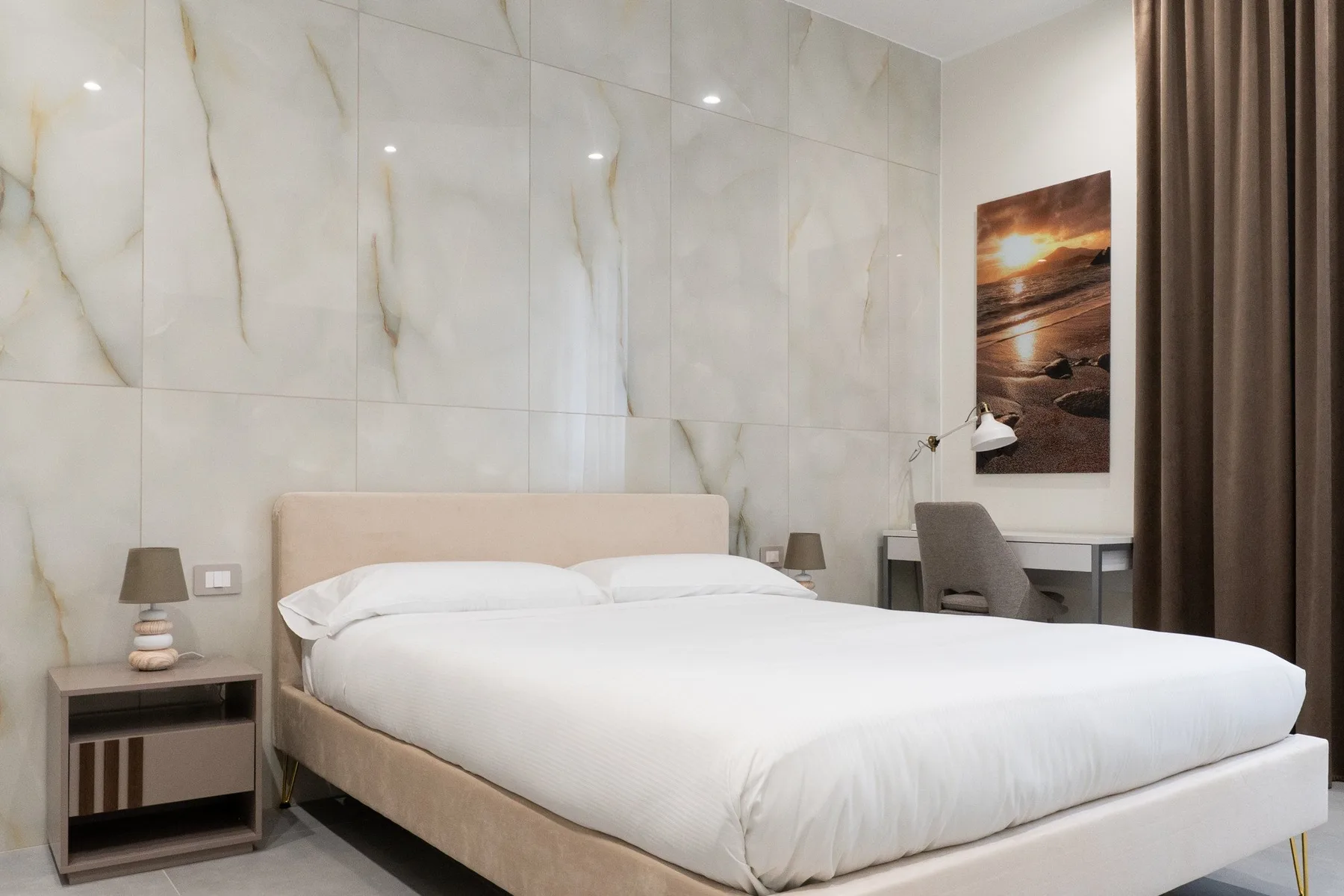 A bedroom with a neatly made bed, bedside tables, and a desk.
