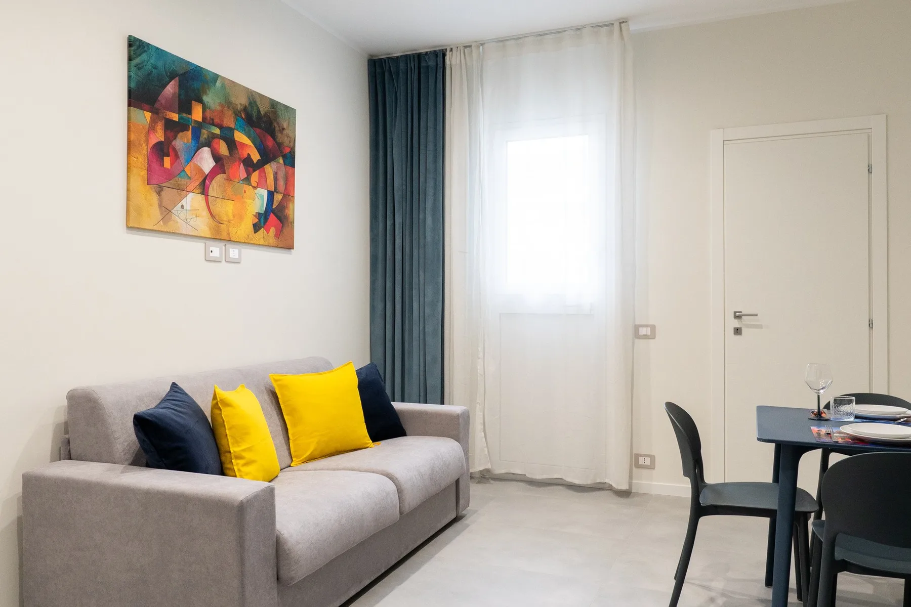 A living and dining area with a gray sofa, colorful cushions, and a table.