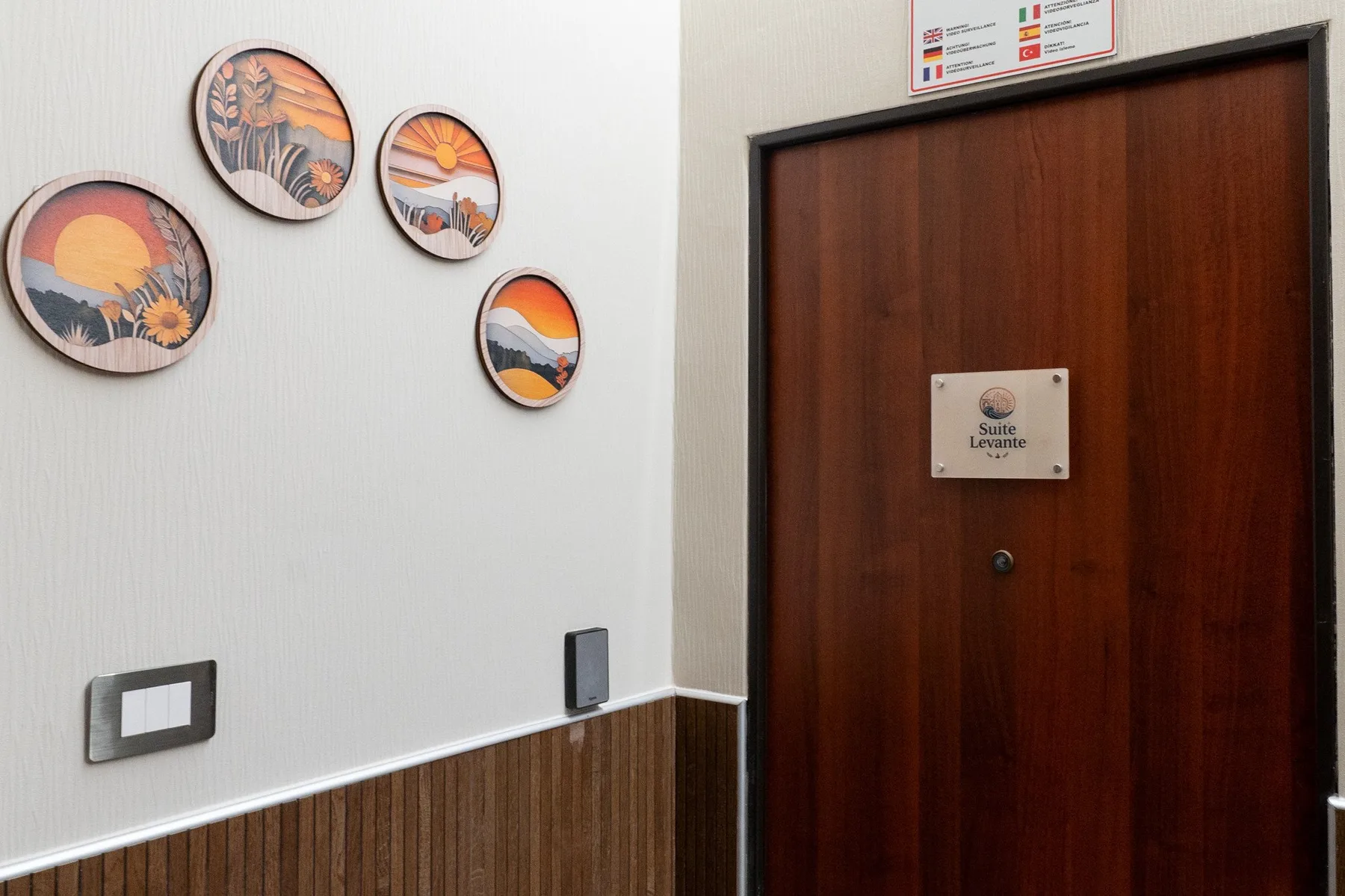 Una puerta de entrada de madera con una pequeña placa está junto a arte mural y un interruptor.