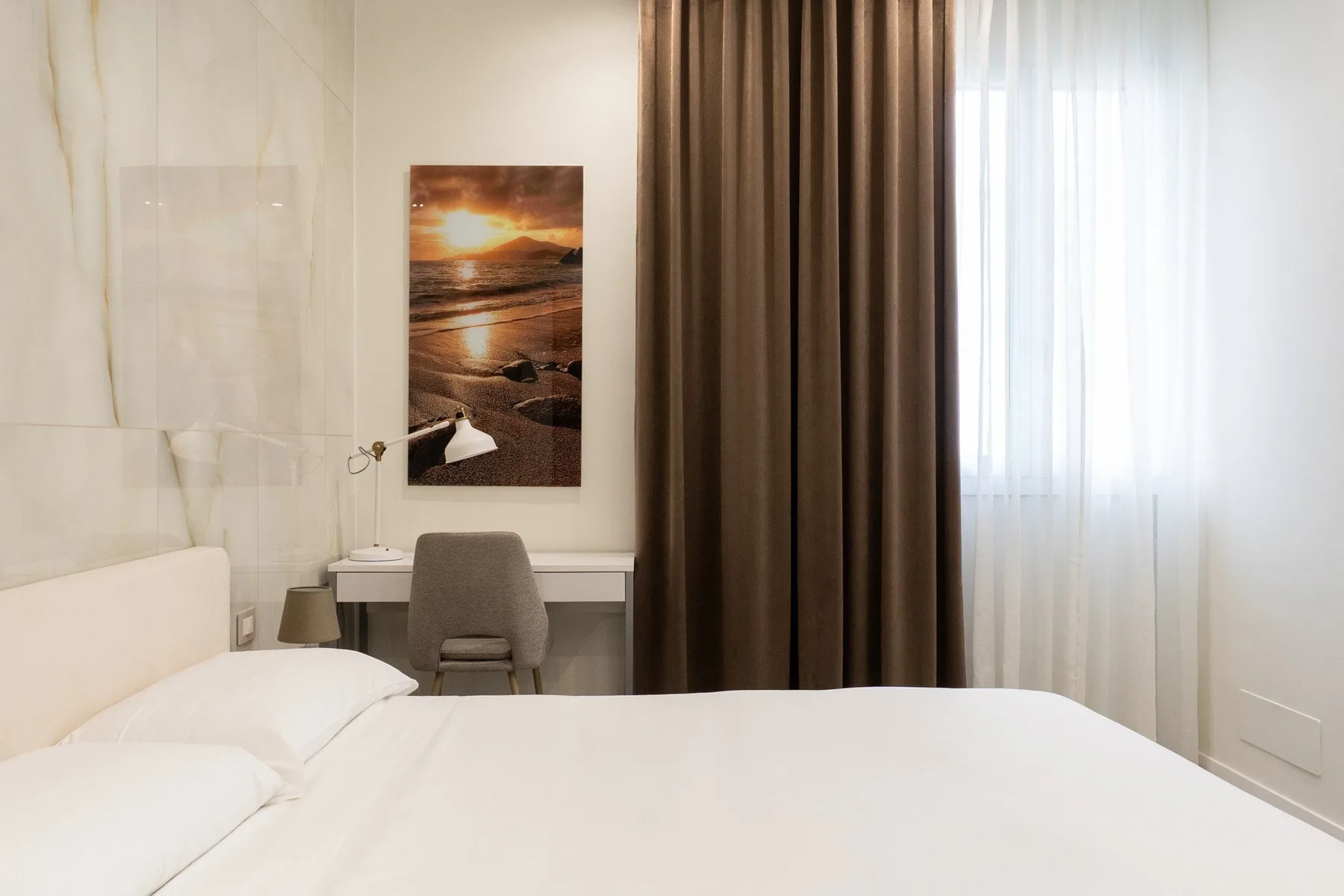 Un dormitorio con una cama bien tendida, un escritorio y cortinas junto a la ventana.
