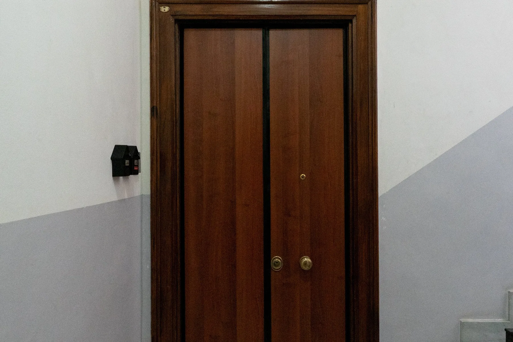Una puerta doble de madera cerrada está en un pasillo con paredes de dos tonos.