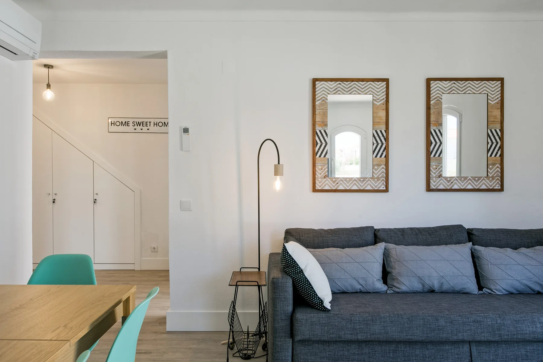 Una sala de estar con un sofá oscuro, espejos en la pared y una mesa de comedor.