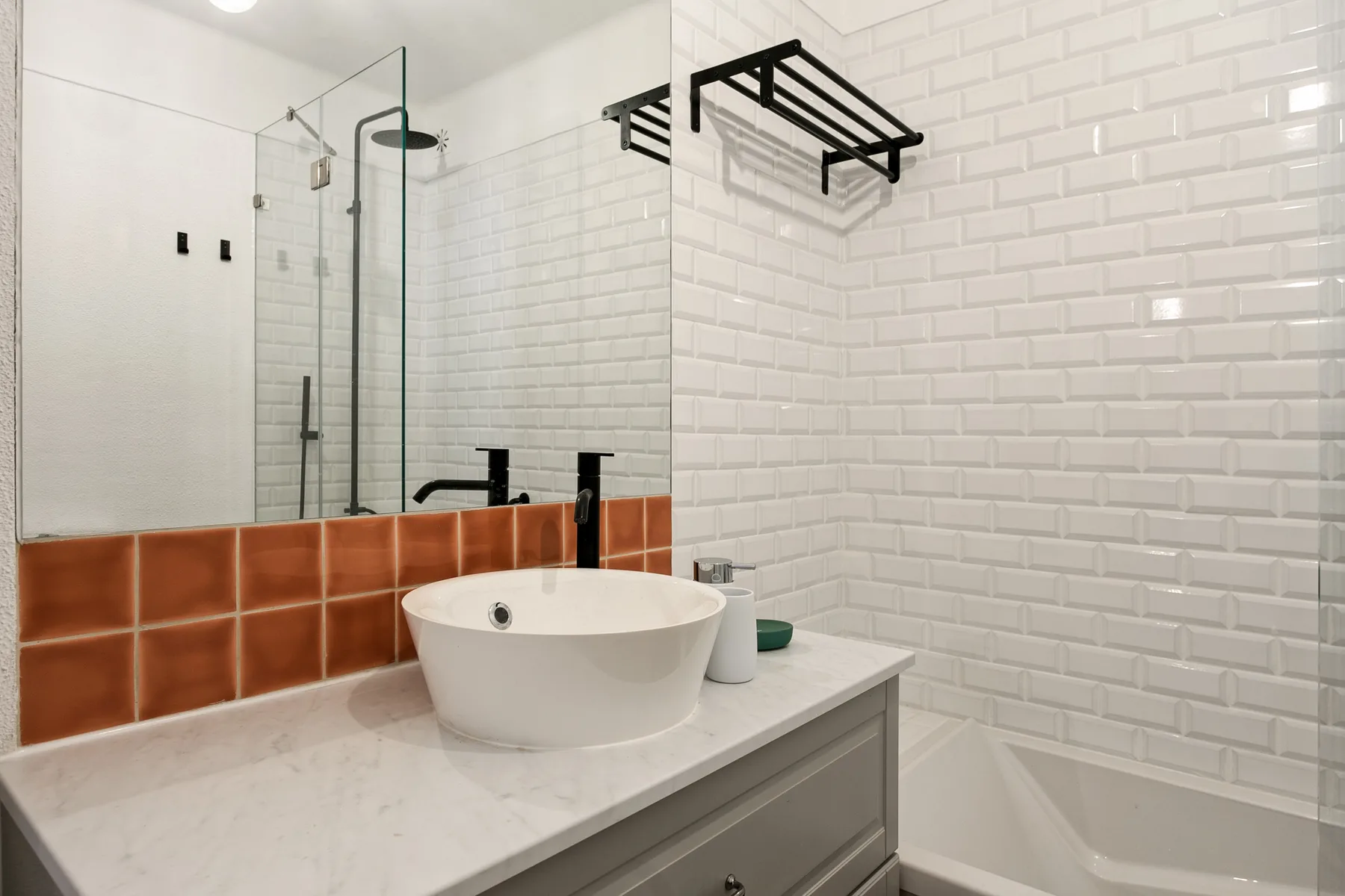 Un baño con azulejos, lavabo blanco sobre la encimera y ducha de vidrio.