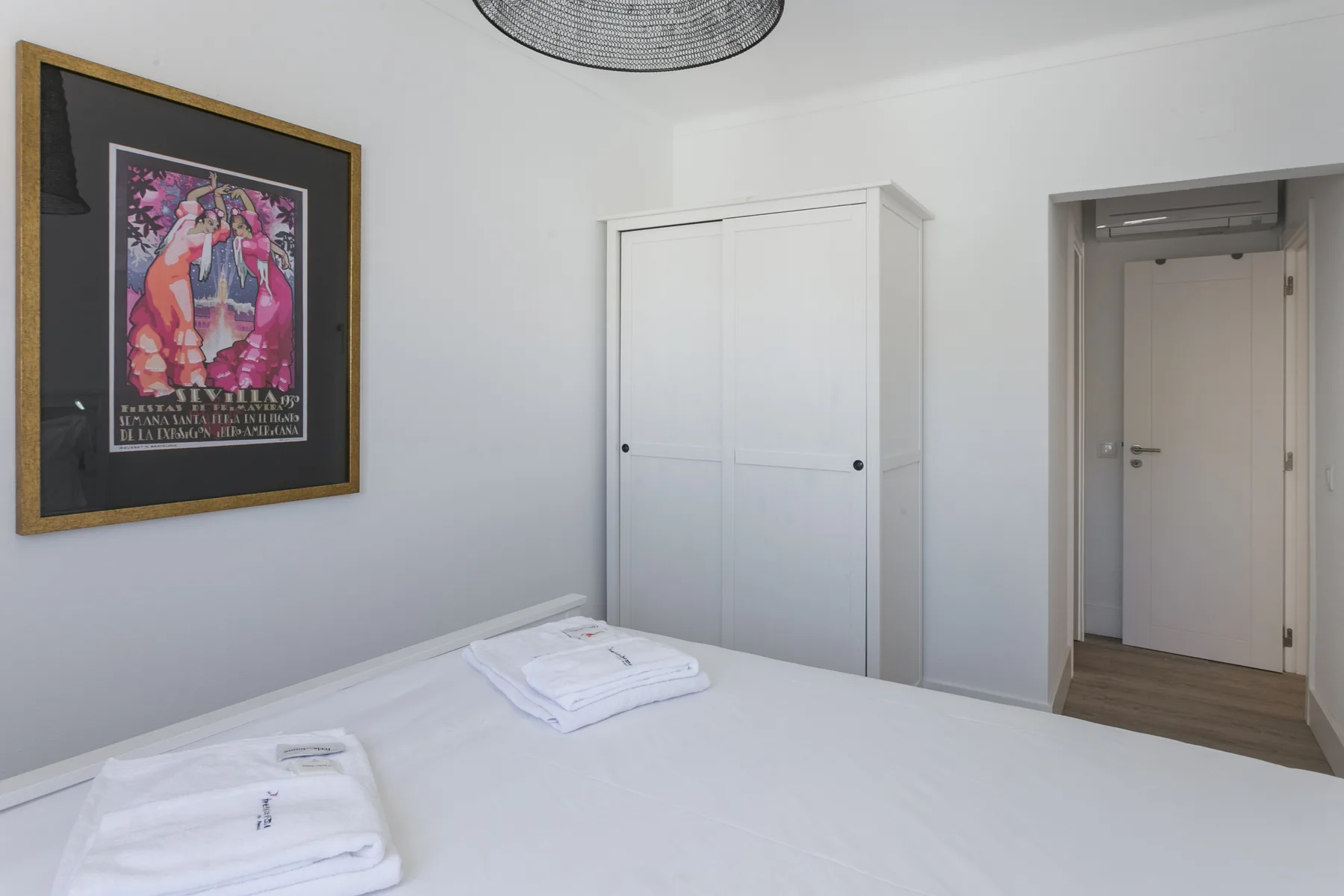 Un dormitorio con la cama arreglada, toallas dobladas y un póster enmarcado.