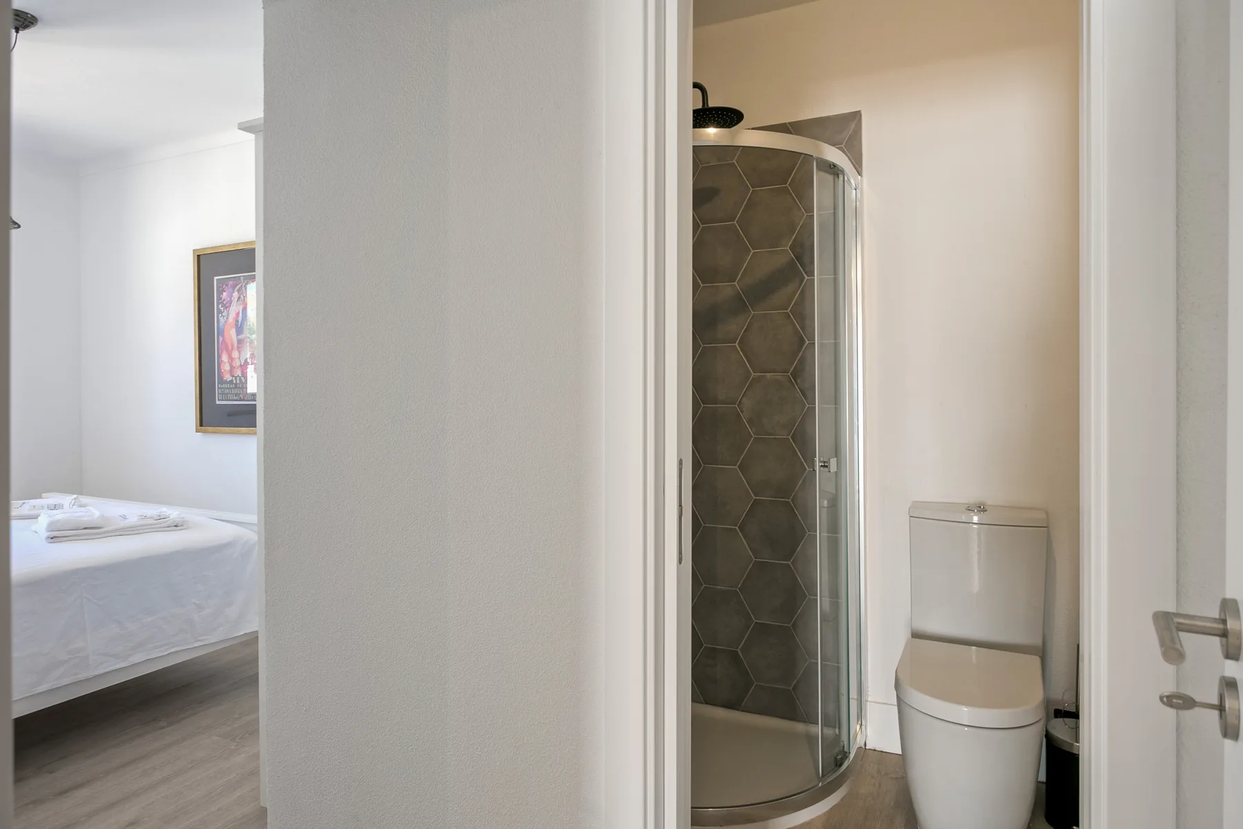 Un baño con ducha de cristal e inodoro, junto a un dormitorio.