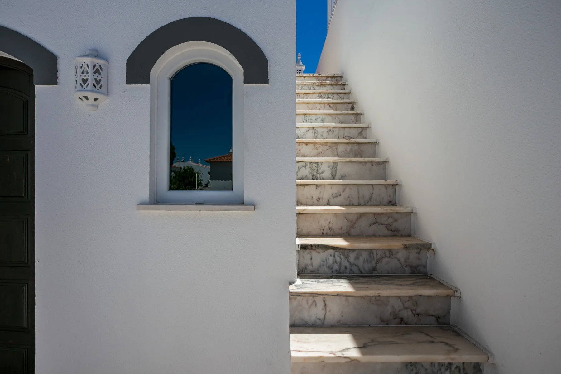 Una pared exterior blanca con una ventana arqueada junto a una escalera de mármol.