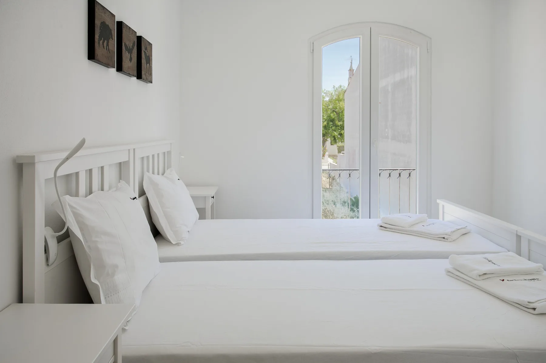 Un dormitorio luminoso con camas blancas y una ventana arqueada.