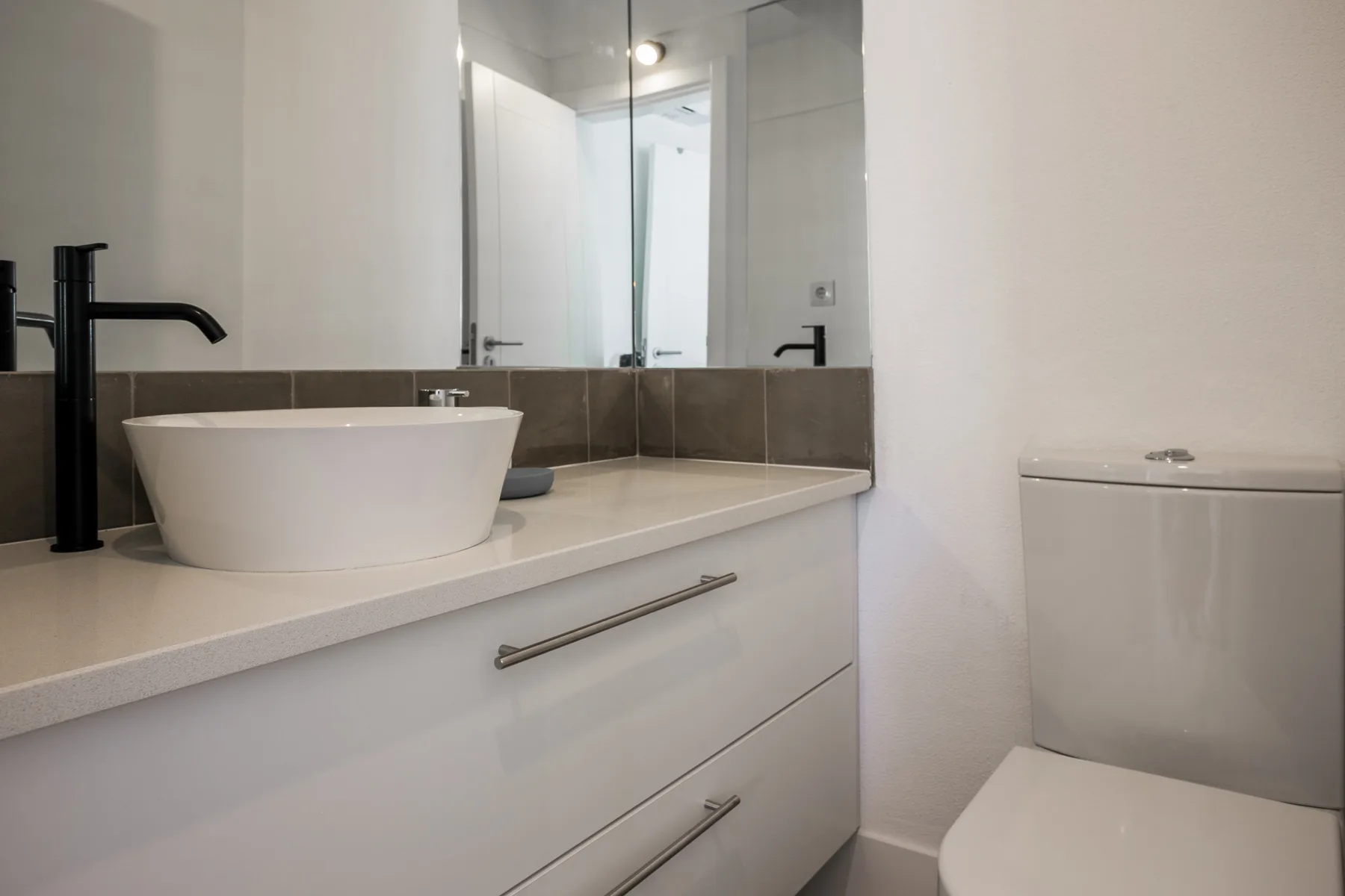 Mueble de baño con lavabo sobre encimera, espejo e inodoro.