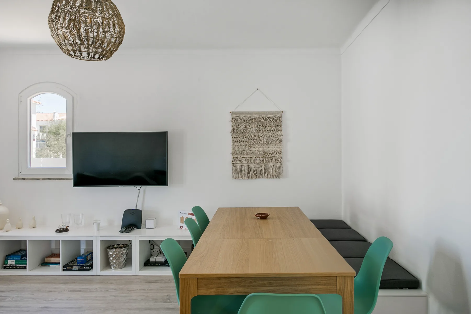 Un comedor con una mesa de madera, sillas verdes y un televisor montado en la pared.