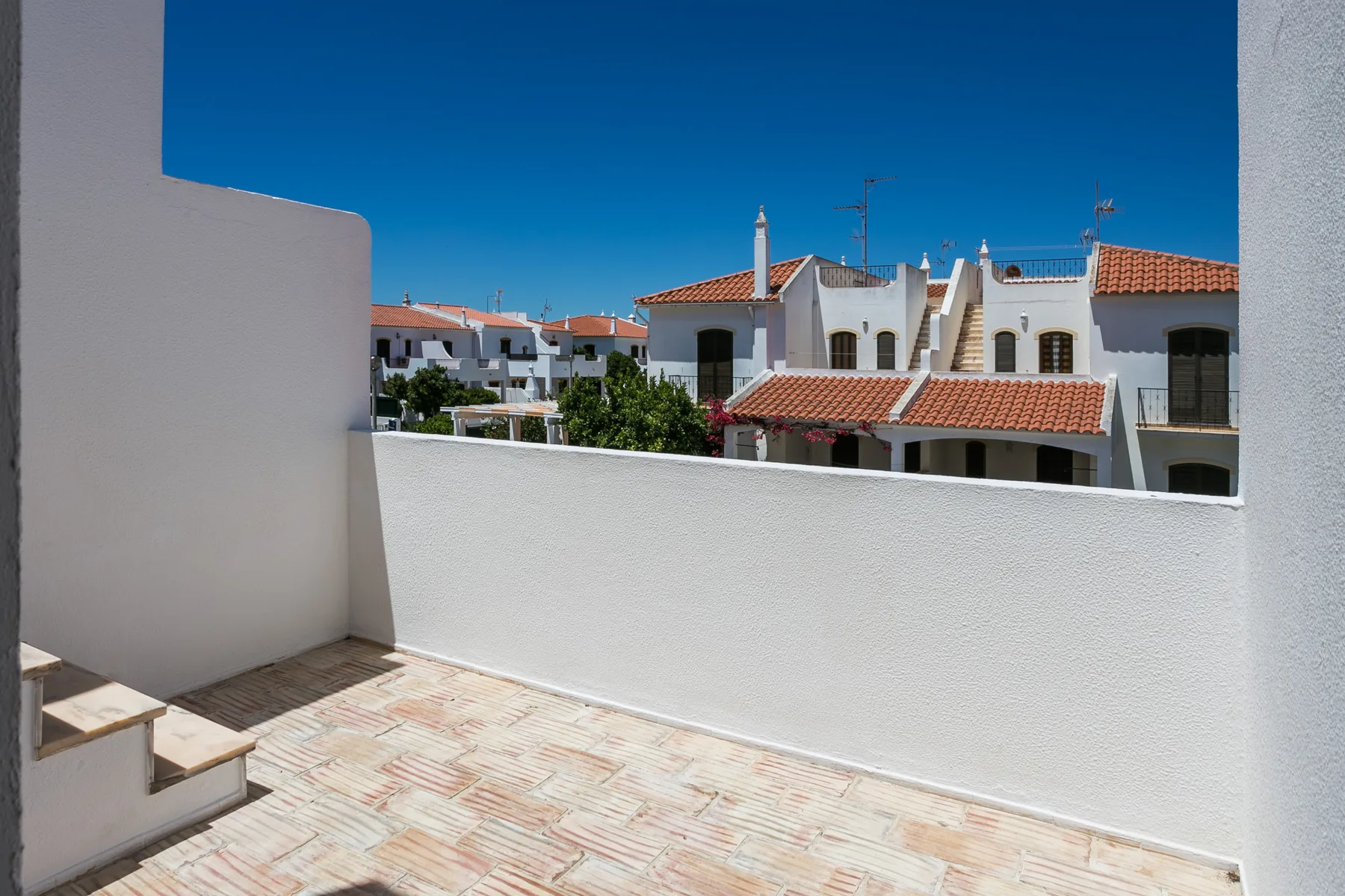 Una terraza soleada da a edificios blancos con tejados de tejas rojas bajo un cielo azul despejado.