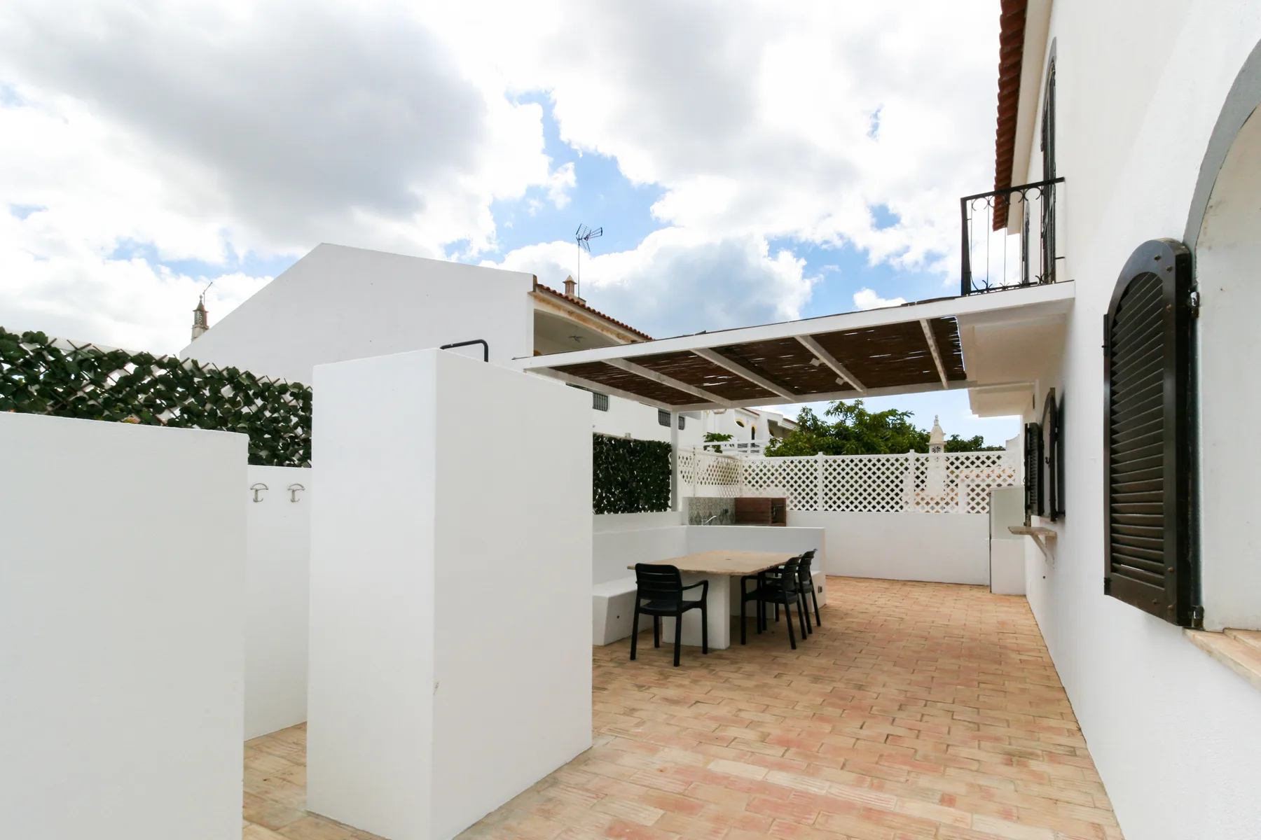 Un patio exterior pavimentado con una zona de comedor cubierta junto a un edificio blanco.