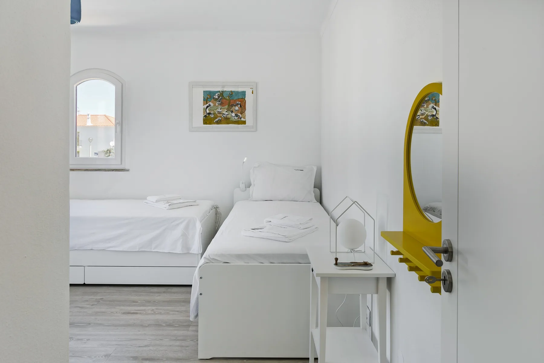 Un dormitorio blanco y luminoso con dos camas y una pequeña mesa auxiliar.