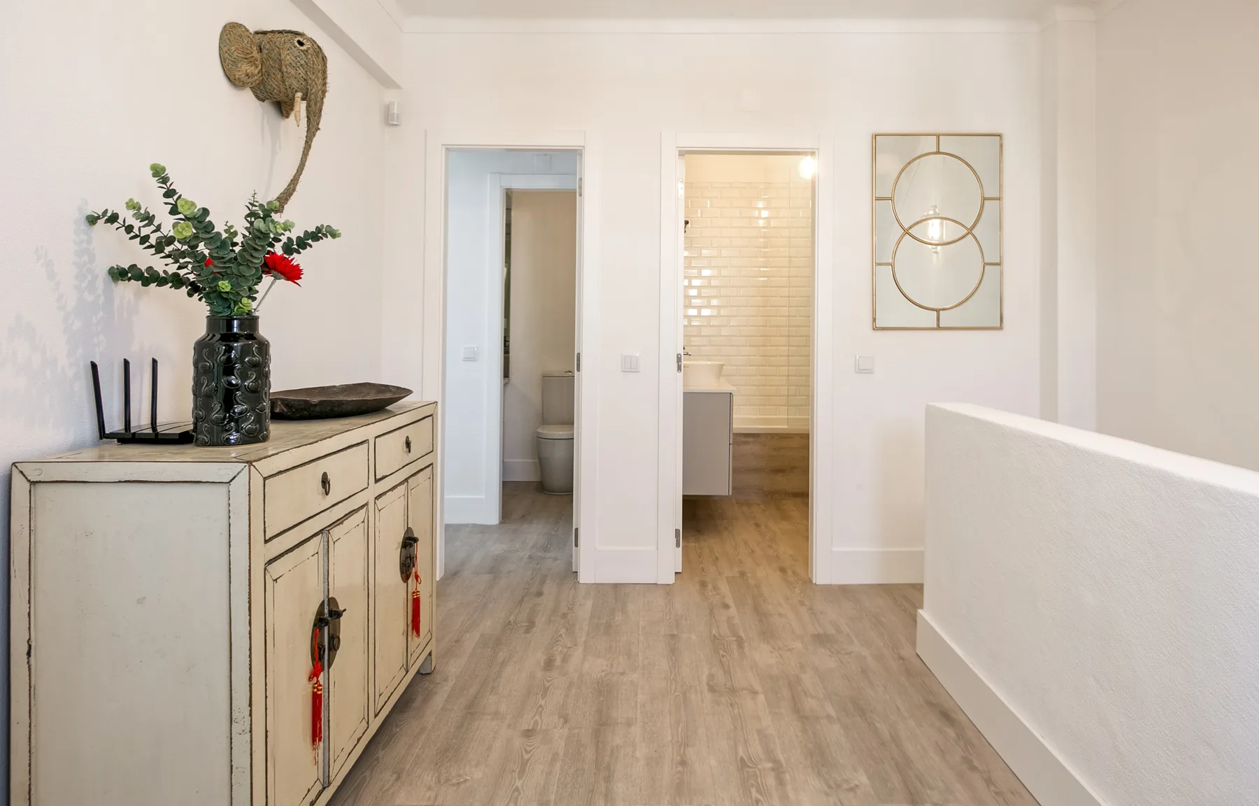 Un pasillo luminoso con un mueble desgastado y puertas que dan a habitaciones contiguas.