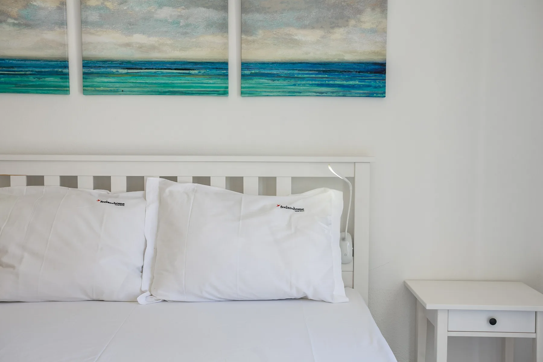 Un dormitorio con ropa de cama blanca y cuadros de temática marina.
