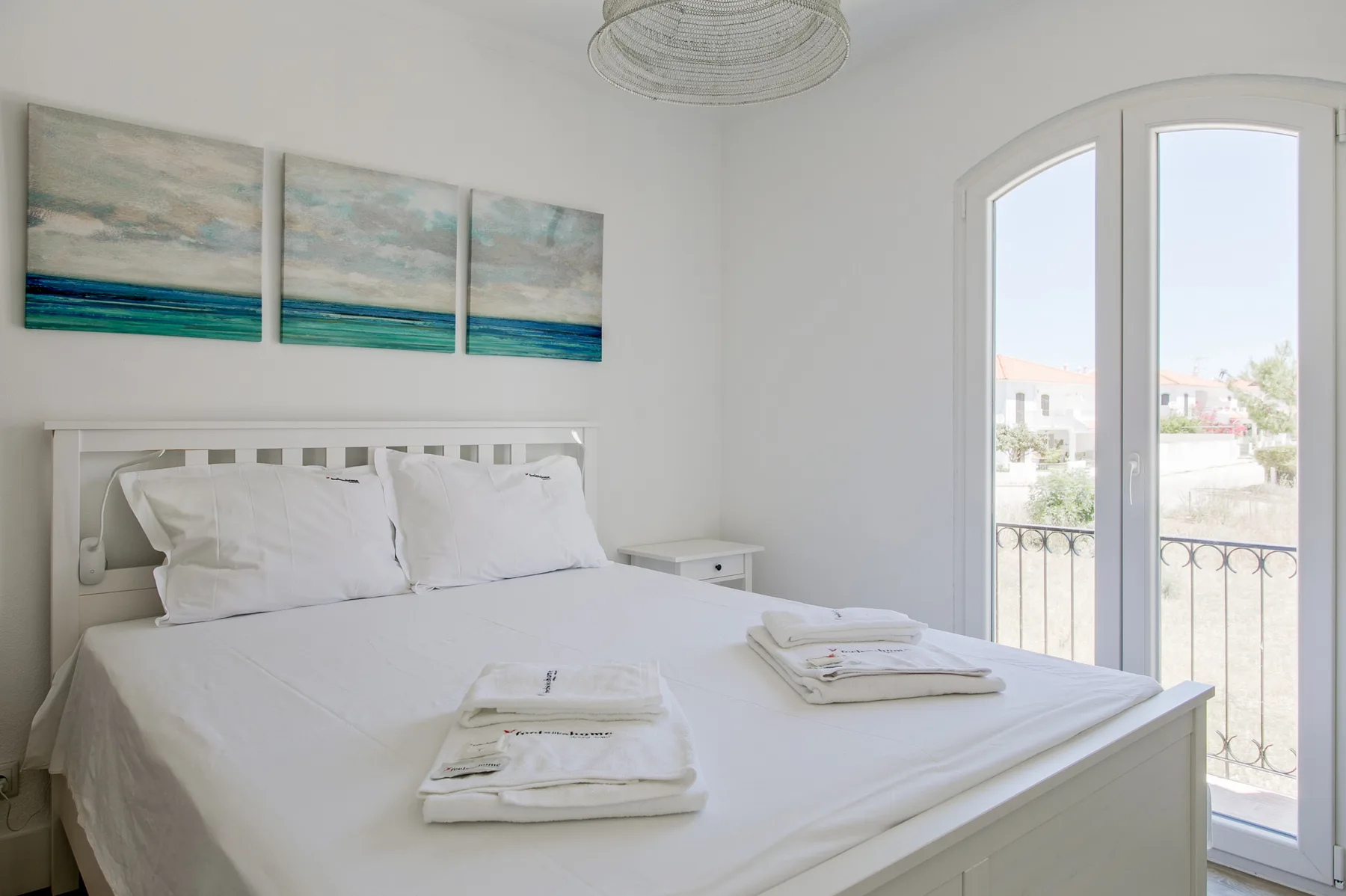 Un dormitorio luminoso con ropa de cama blanca y cuadros sobre la cama.
