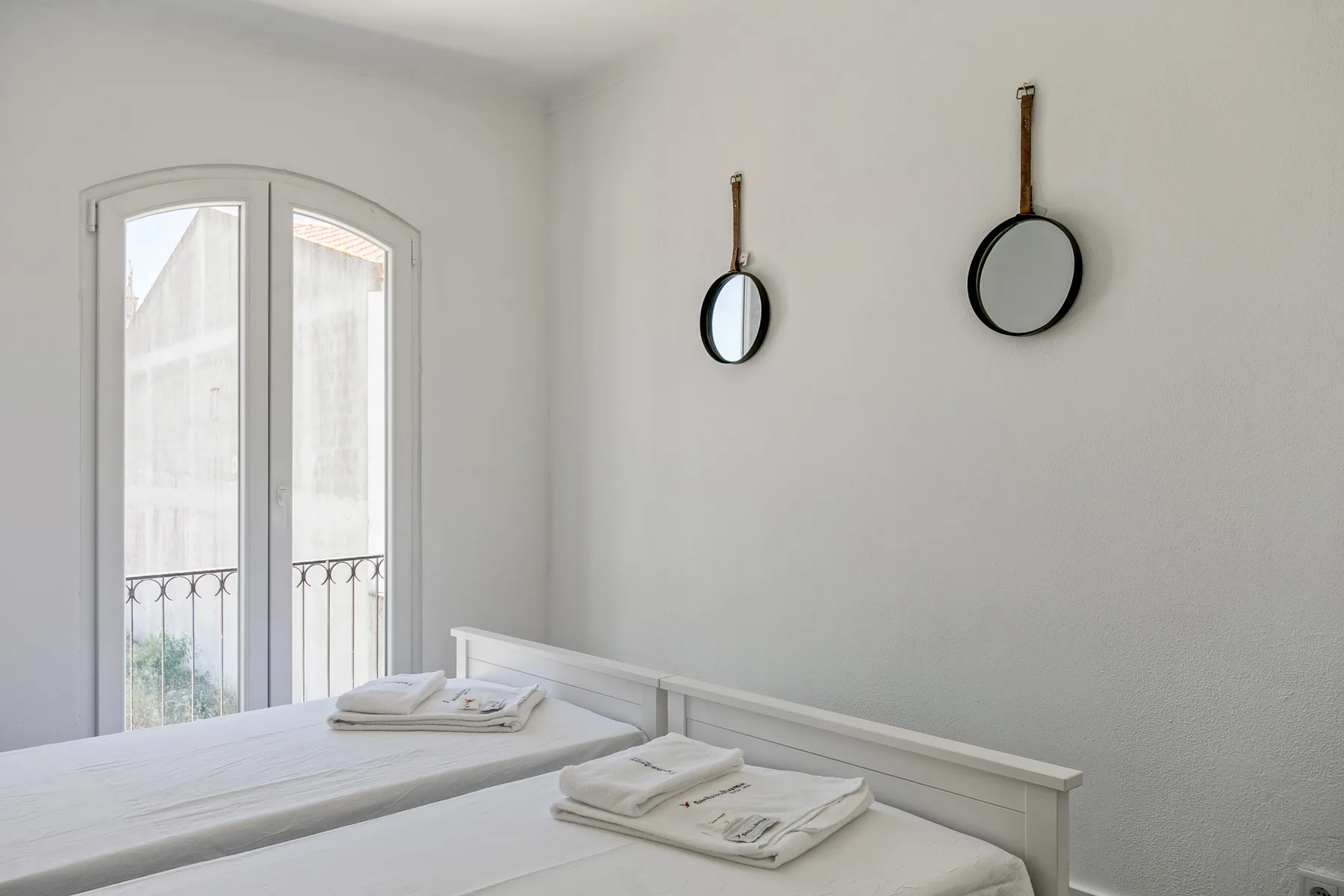 Un dormitorio luminoso con ropa de cama blanca y dos espejos redondos en la pared.