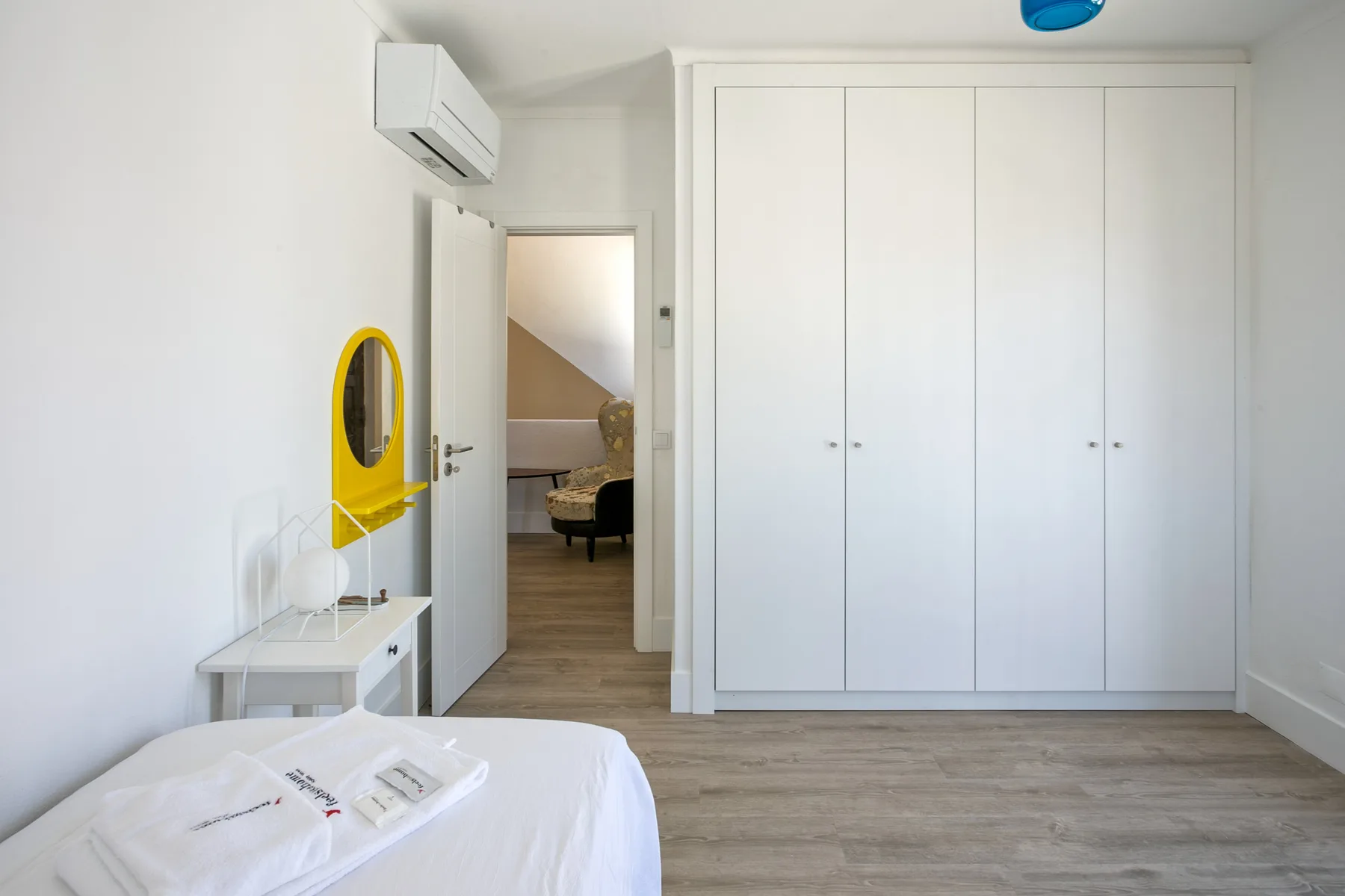 Un dormitorio luminoso con una cama, armarios blancos y una puerta abierta.