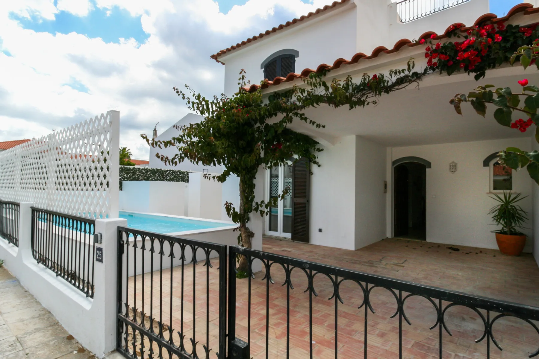 Una casa blanca con una pequeña piscina, patio de baldosas y enredaderas floridas sobre la entrada.