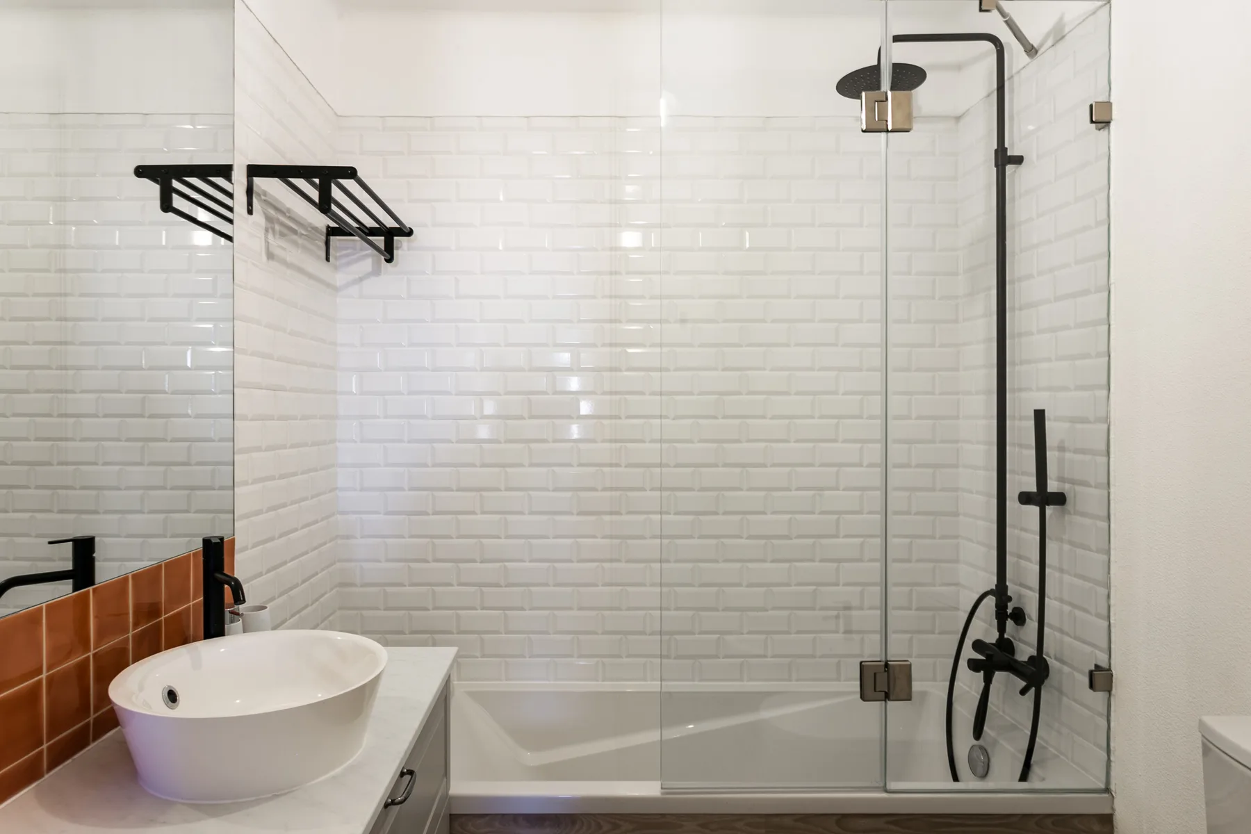 Un baño alicatado con bañera, mampara de vidrio y lavabo sobre encimera.