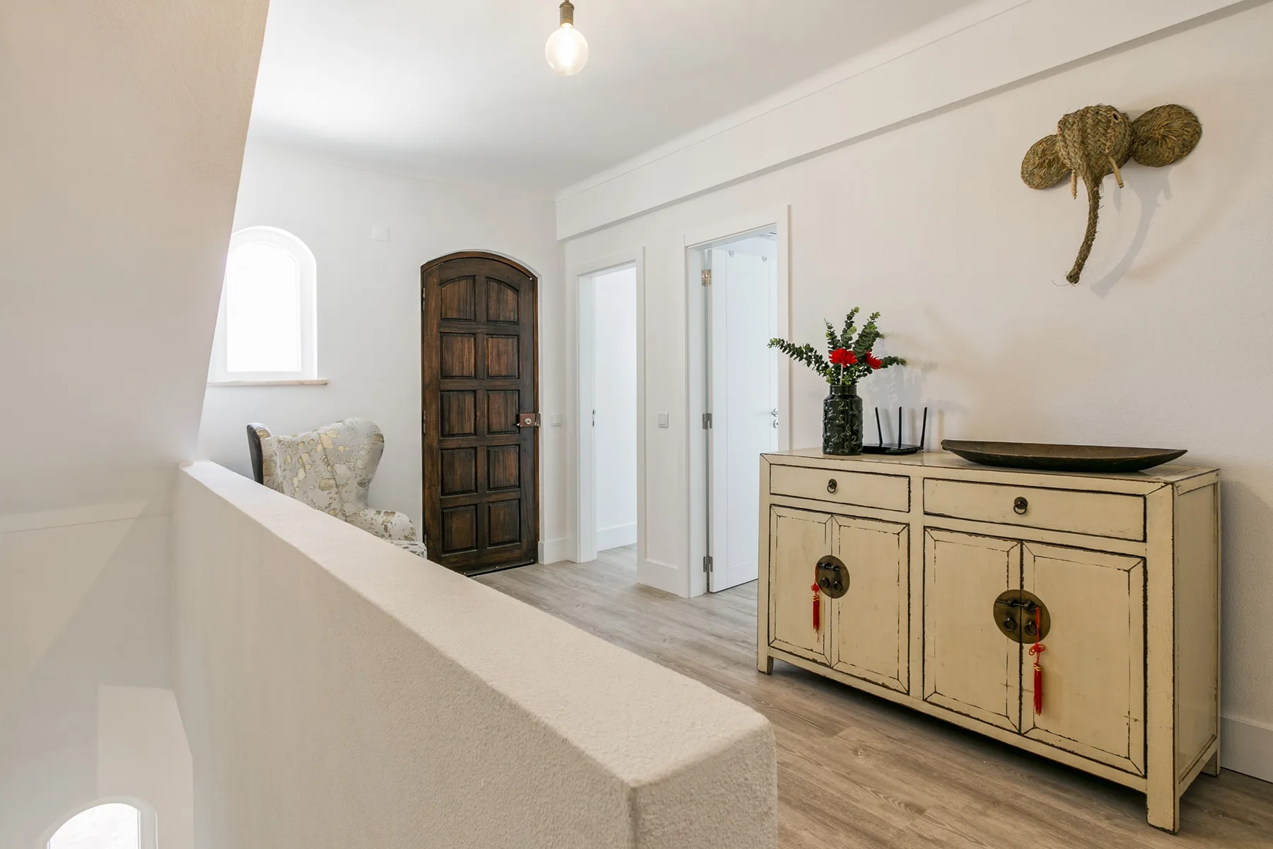 Un pasillo luminoso con una puerta de madera, un aparador claro y flores.