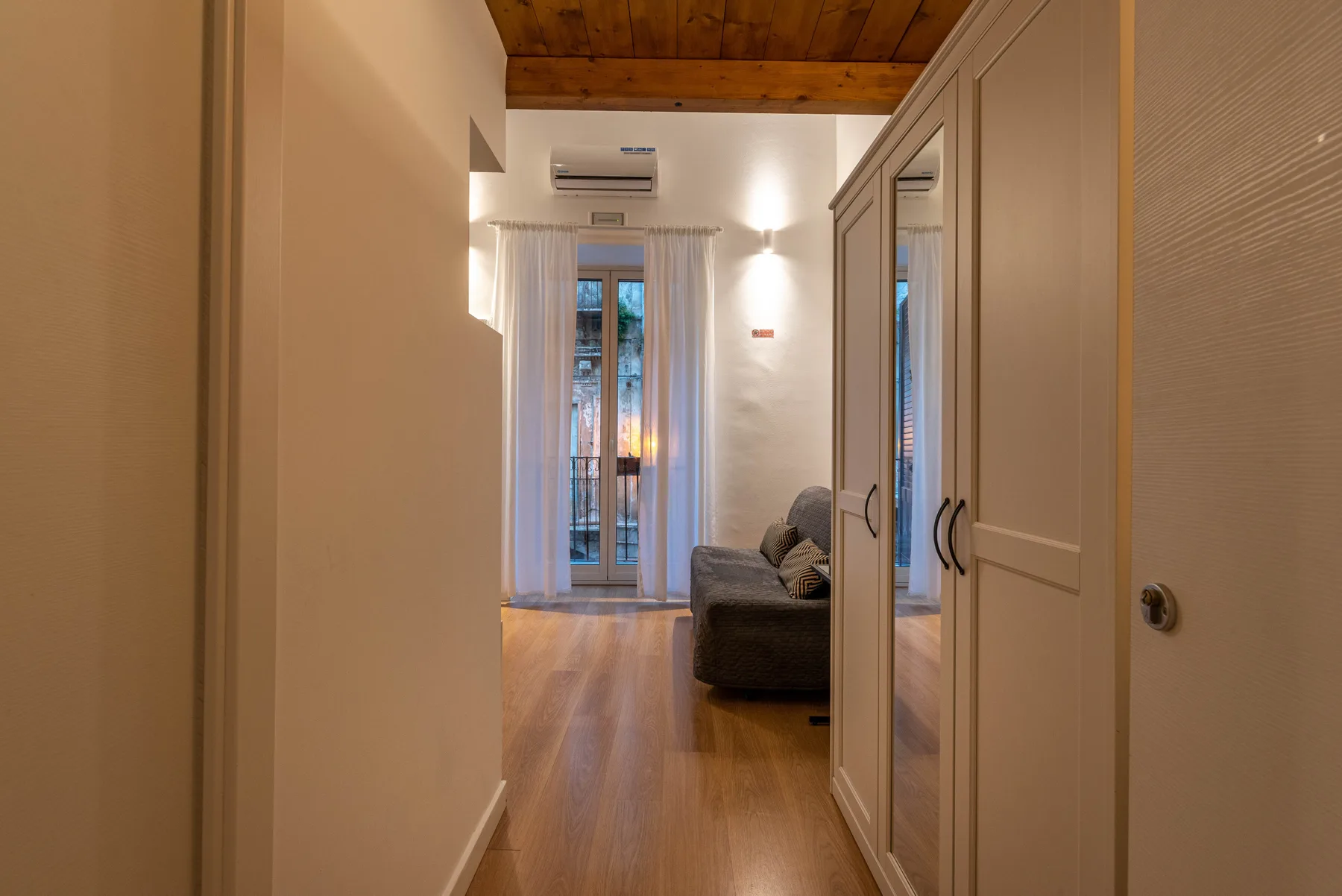 A hallway opens toward a seating area and tall curtained windows.