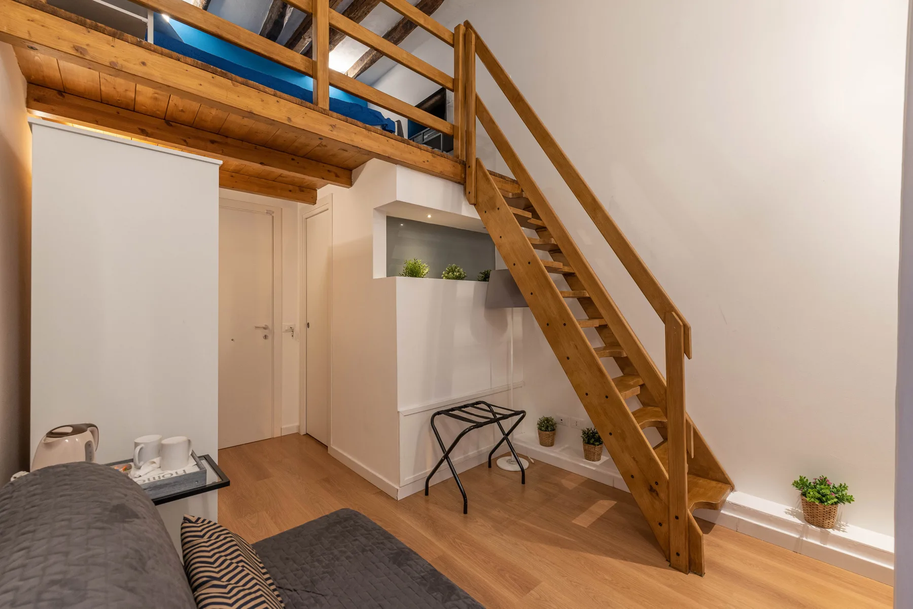A compact bedroom with a wooden loft staircase and built-in wall shelves.