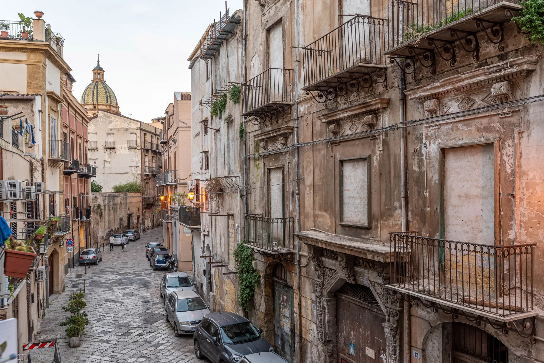 A narrow cobblestone street lined with old buildings and parked cars.