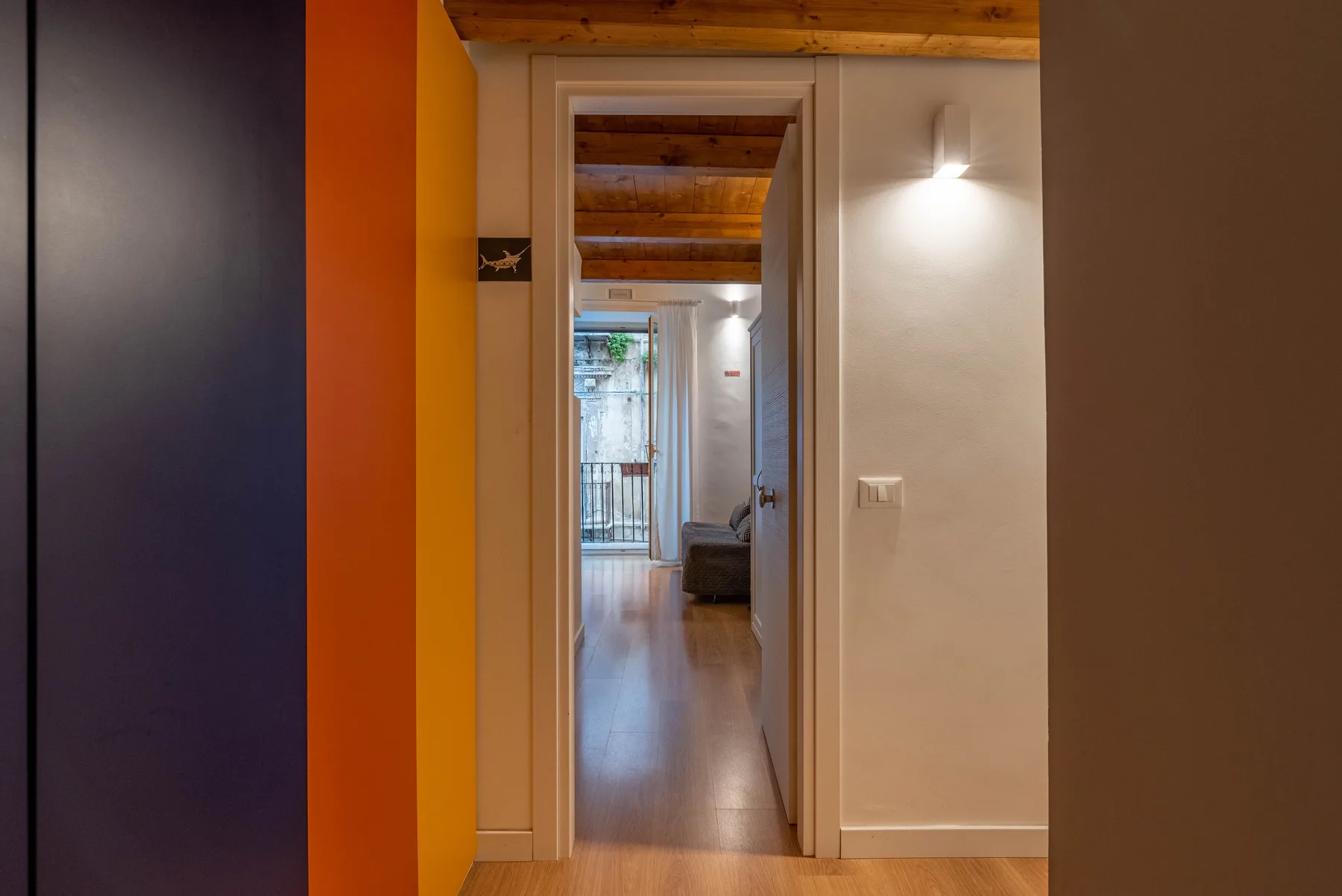 A hallway leads toward a bright room with a glass balcony door.