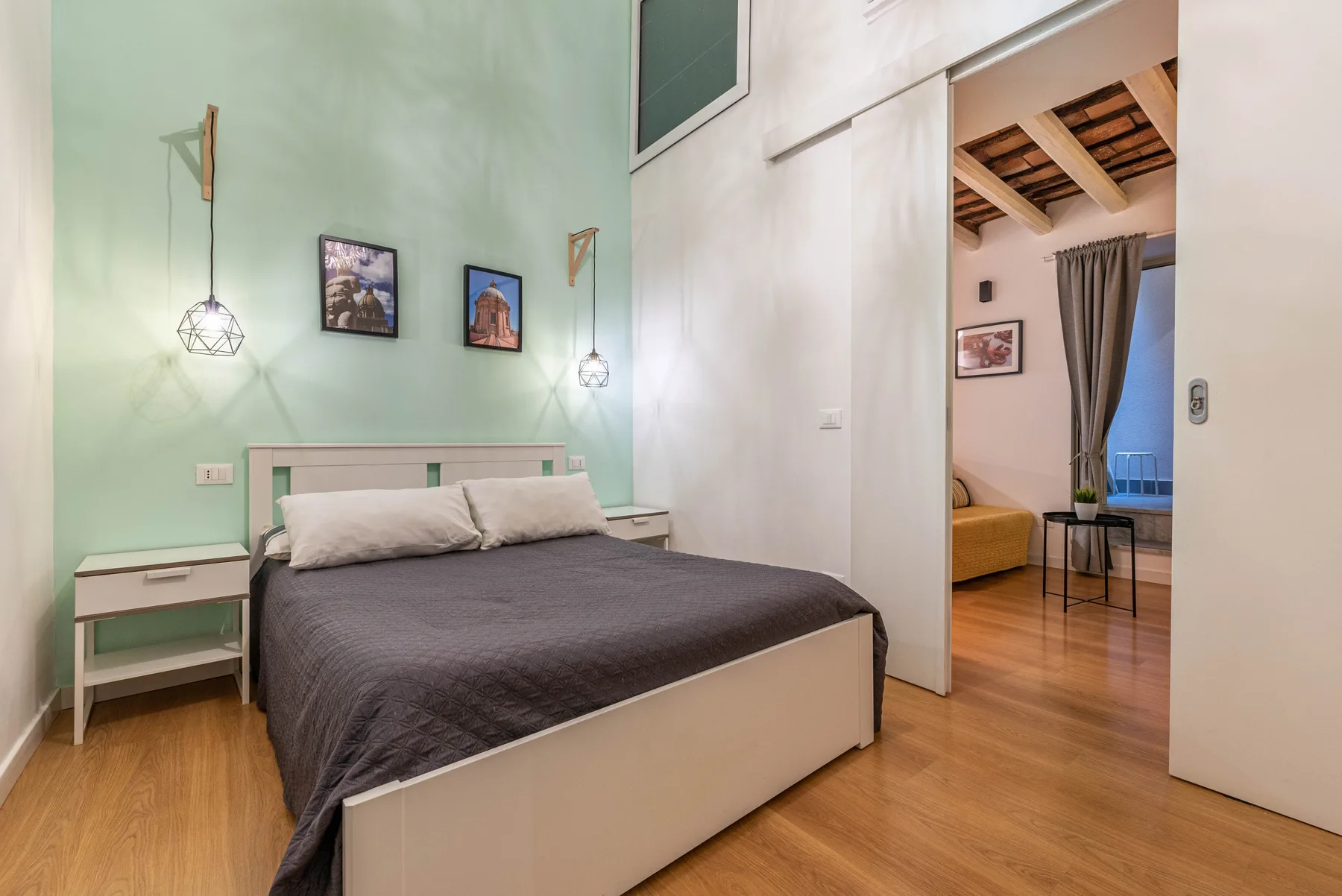 A bedroom with a bed and bedside tables, opening into an adjoining sitting area.