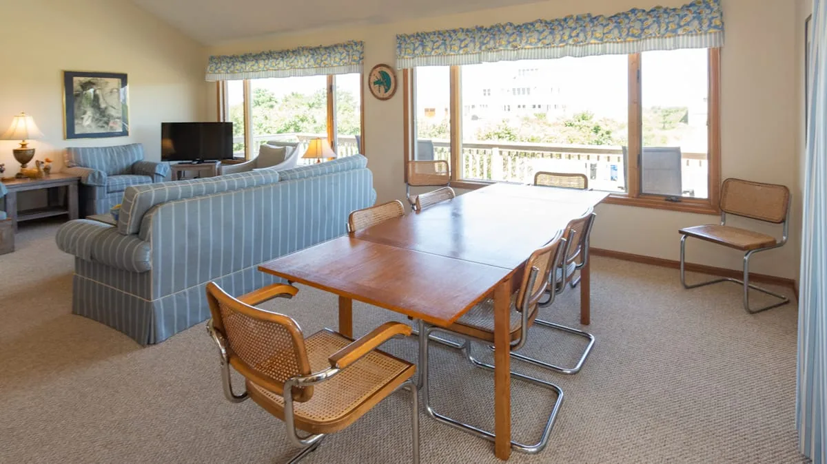 Comedor con una mesa larga de madera y asientos junto a grandes ventanas.
