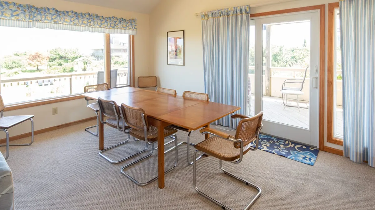 Un comedor con una mesa de madera y sillas junto a grandes ventanas.