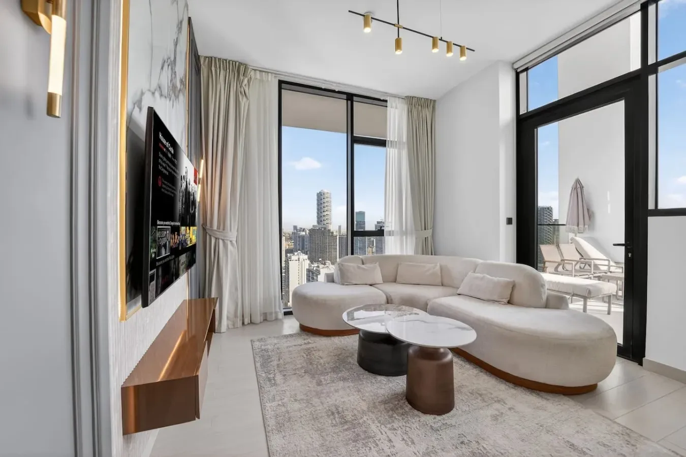 A bright living room with curved seating, coffee tables, and large windows overlooking the city.