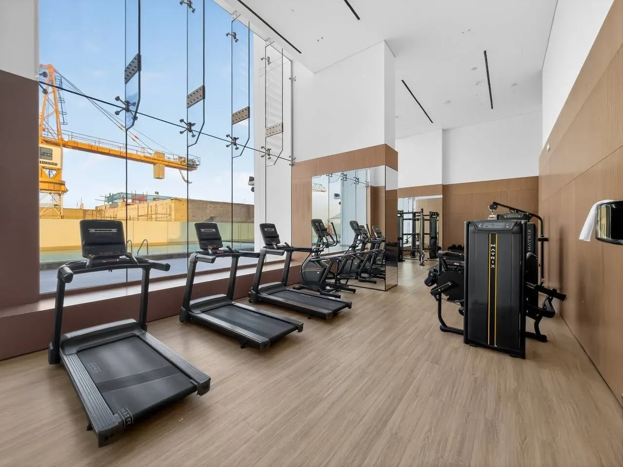 A gym with treadmills and exercise equipment beside large windows.