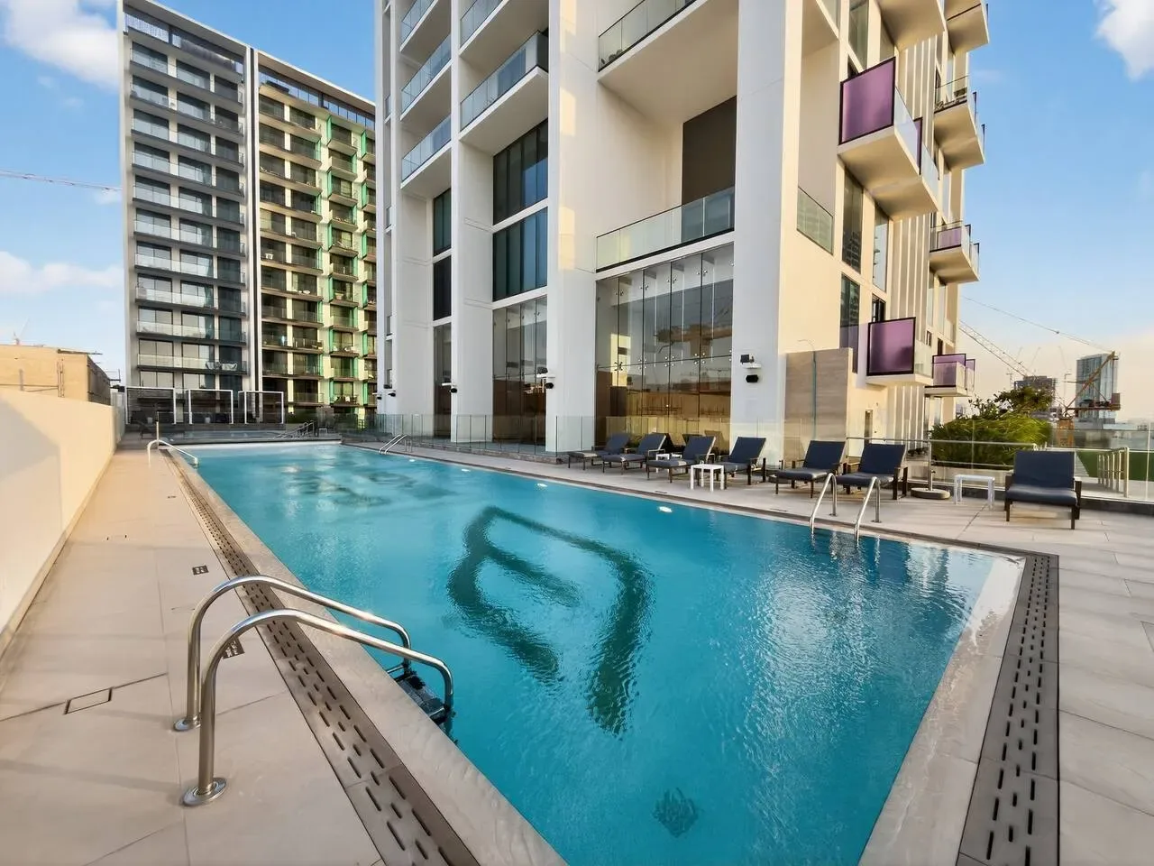 An outdoor swimming pool beside modern apartment buildings and lounge seating.