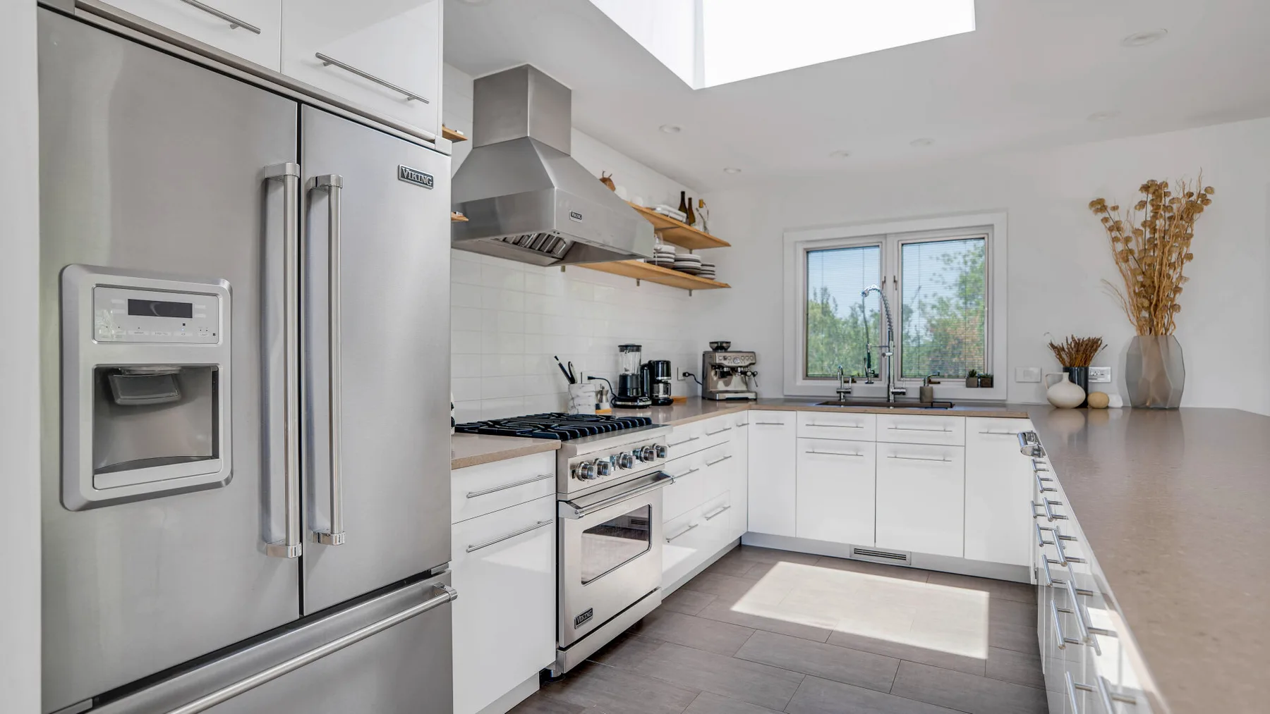 A bright kitchen with white cabinets, stainless steel appliances, and a large window.