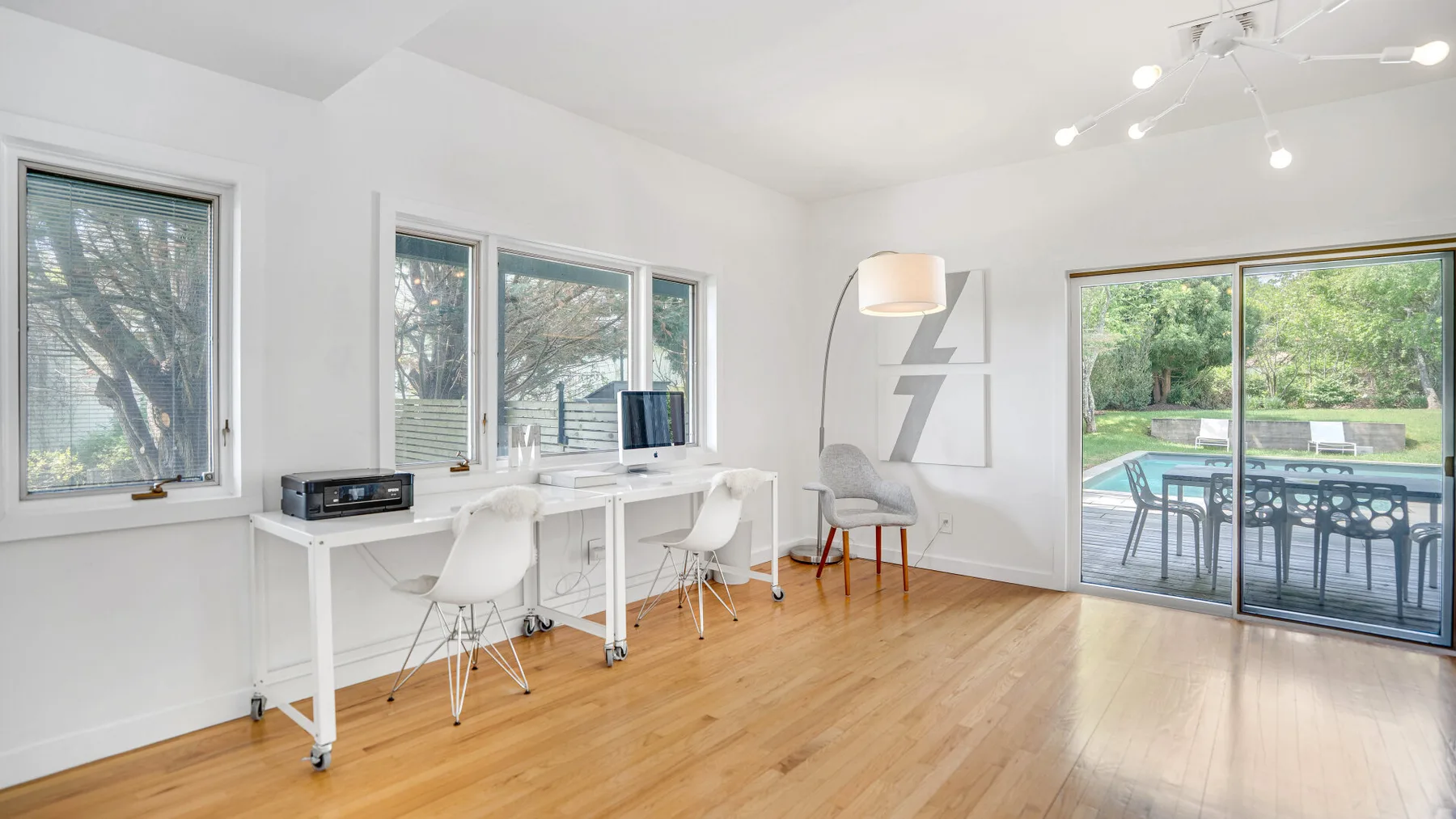 A bright workspace with a long white desk beside large windows overlooking a garden.