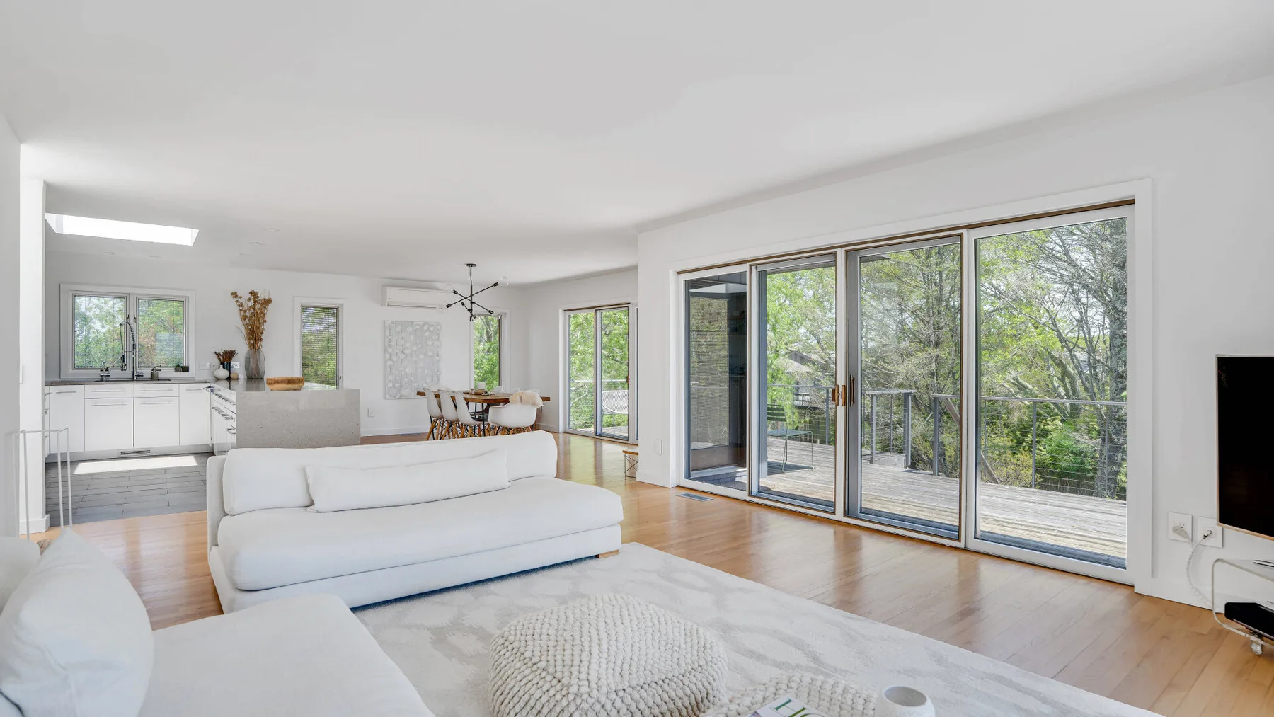 A bright living room with white seating and large windows overlooking greenery.