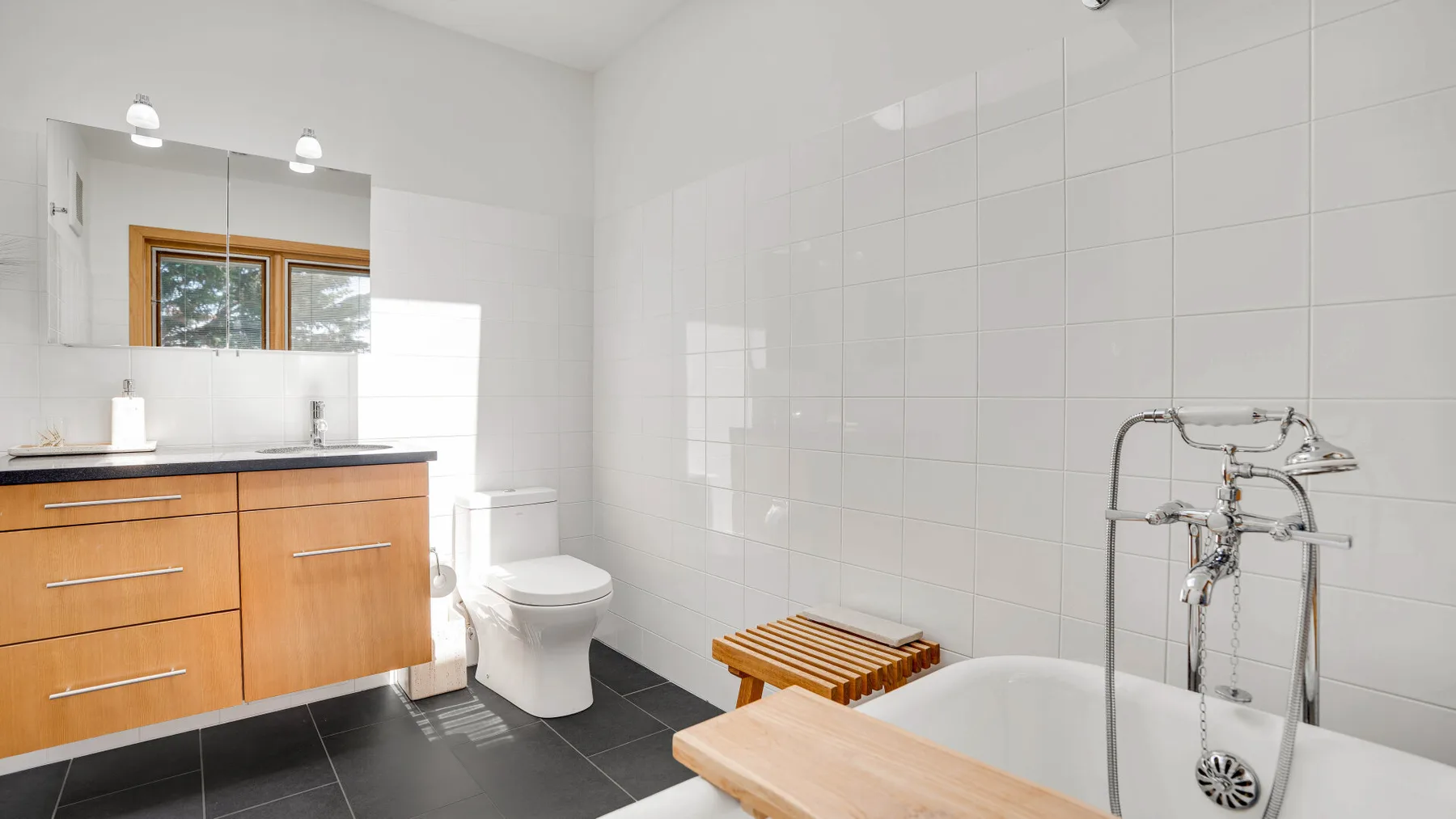 A bright bathroom with a bathtub, tiled walls, and a wood vanity.
