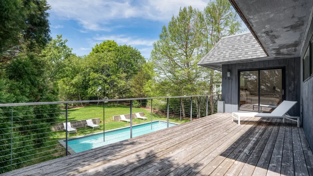 A wooden deck overlooks a swimming pool surrounded by trees.