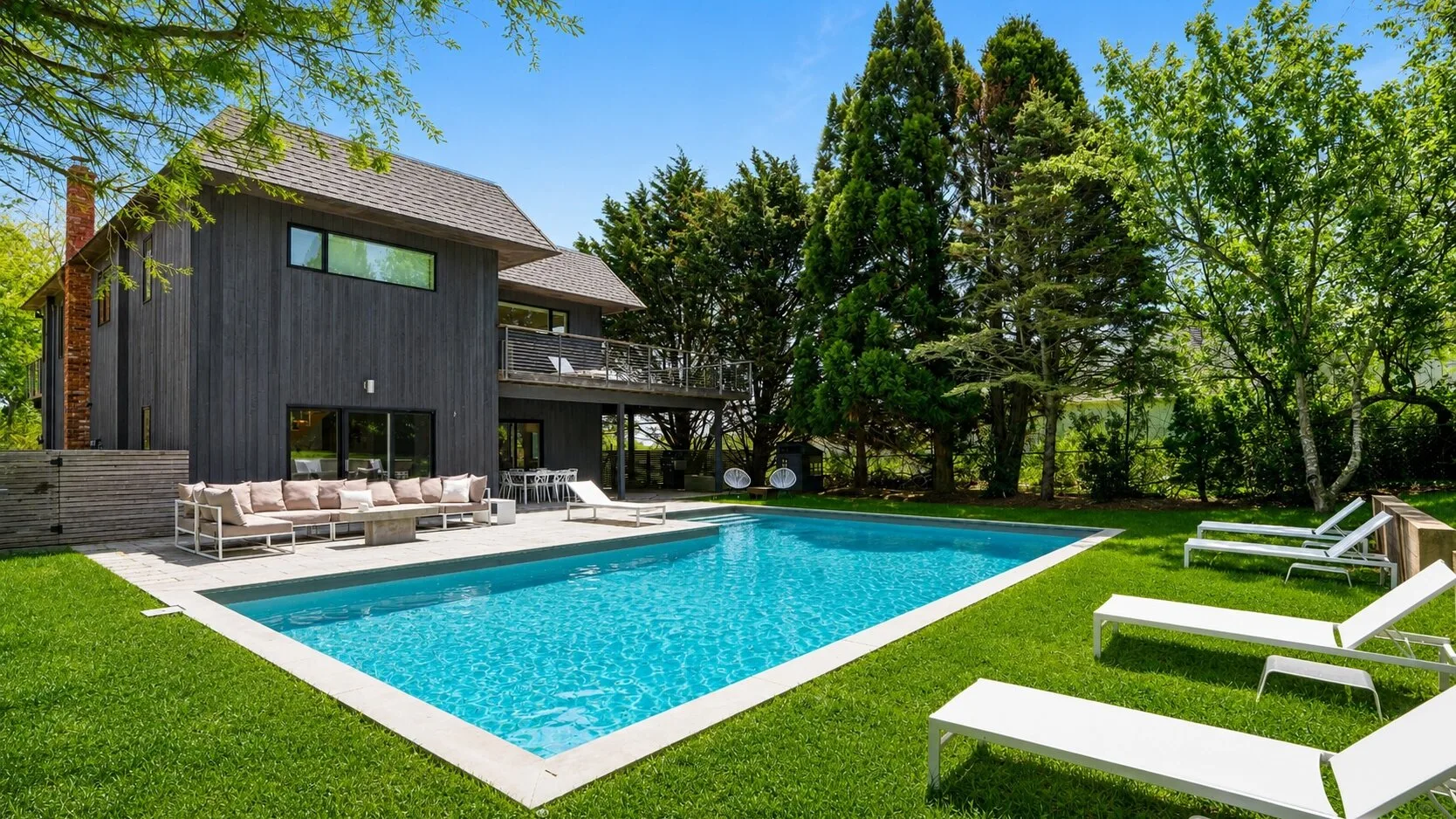 Una piscina junto a una casa moderna, con tumbonas sobre el césped.