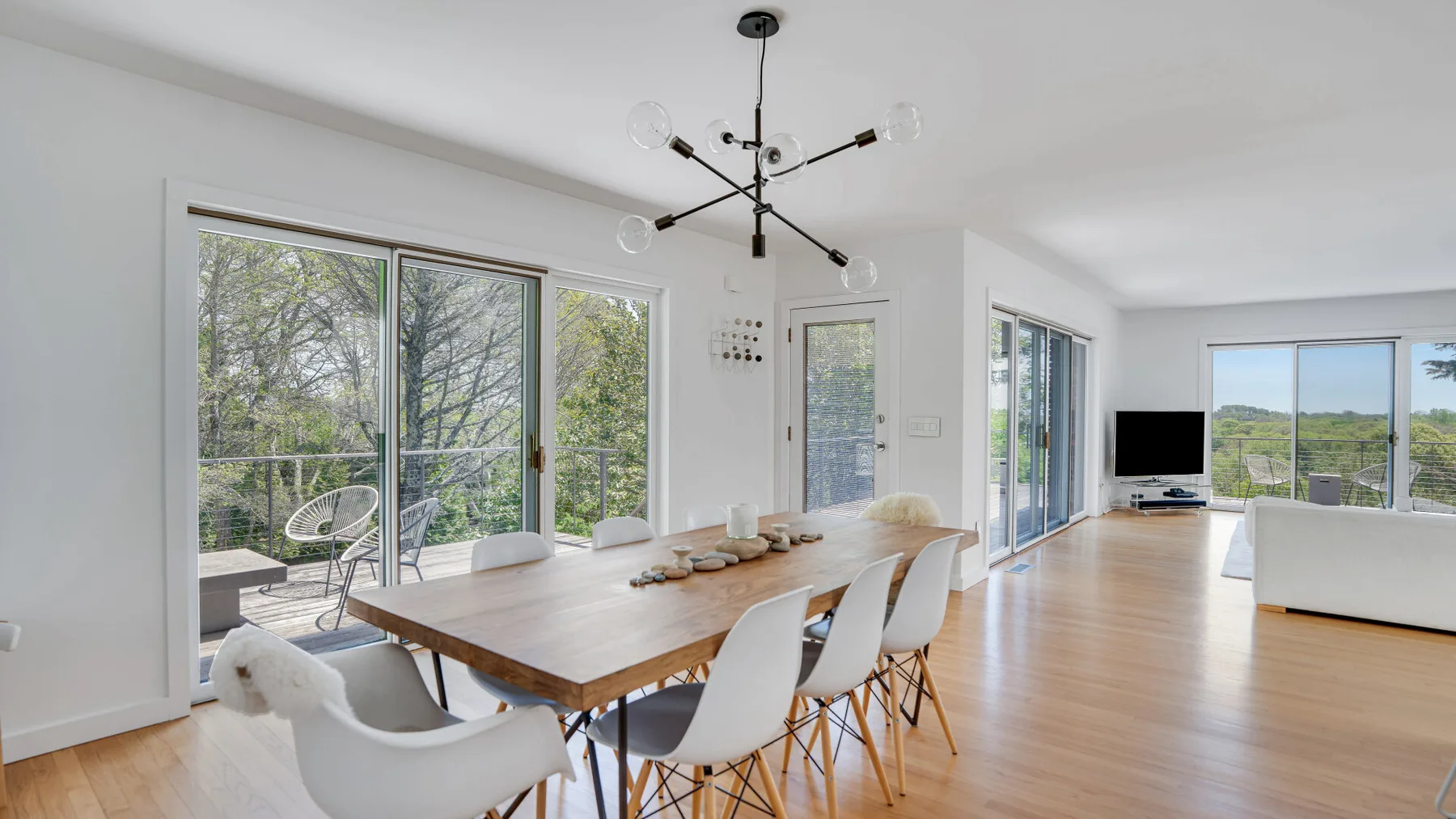 A bright open-plan living and dining area has large windows and a long dining table.