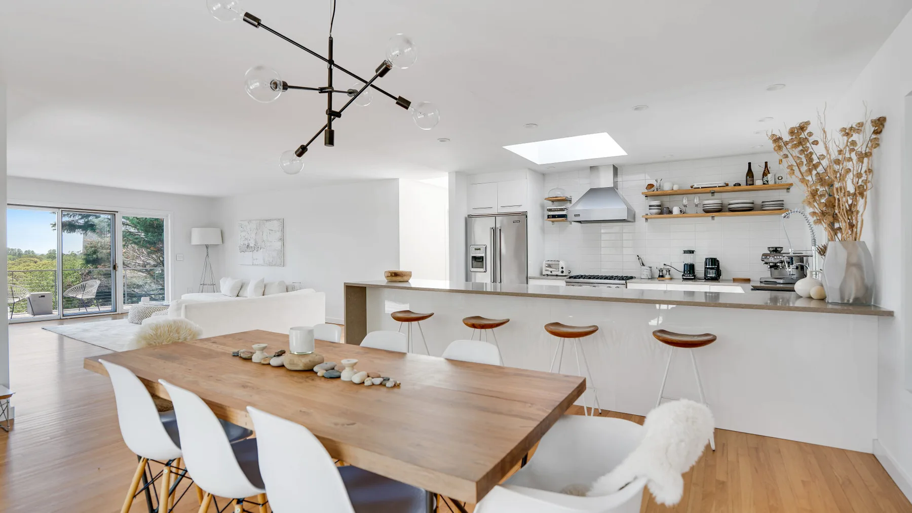 A bright open-plan kitchen and dining area, with a long wooden table beside the kitchen island.