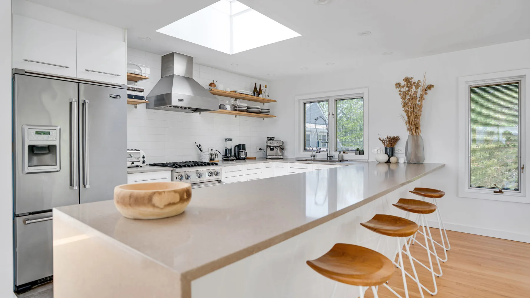 A bright kitchen with a long island and wooden bar stools.