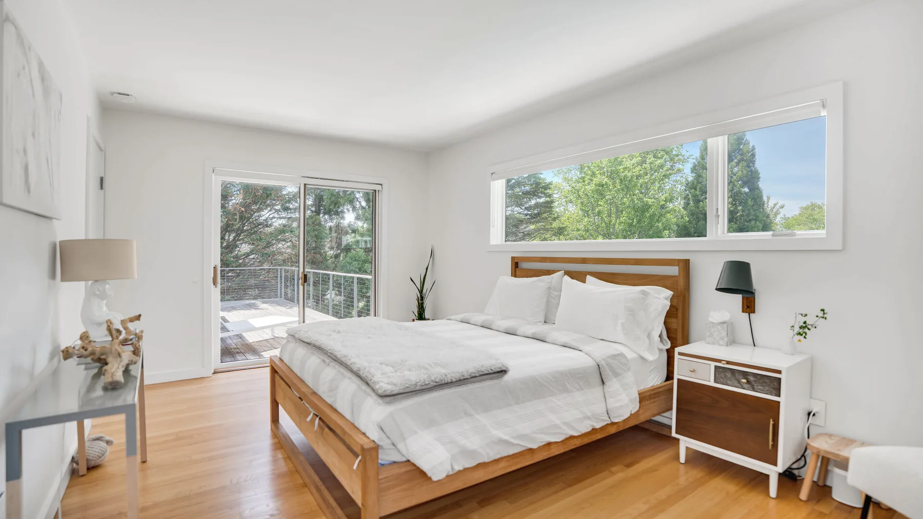 A bright bedroom with a wooden bed and large windows.