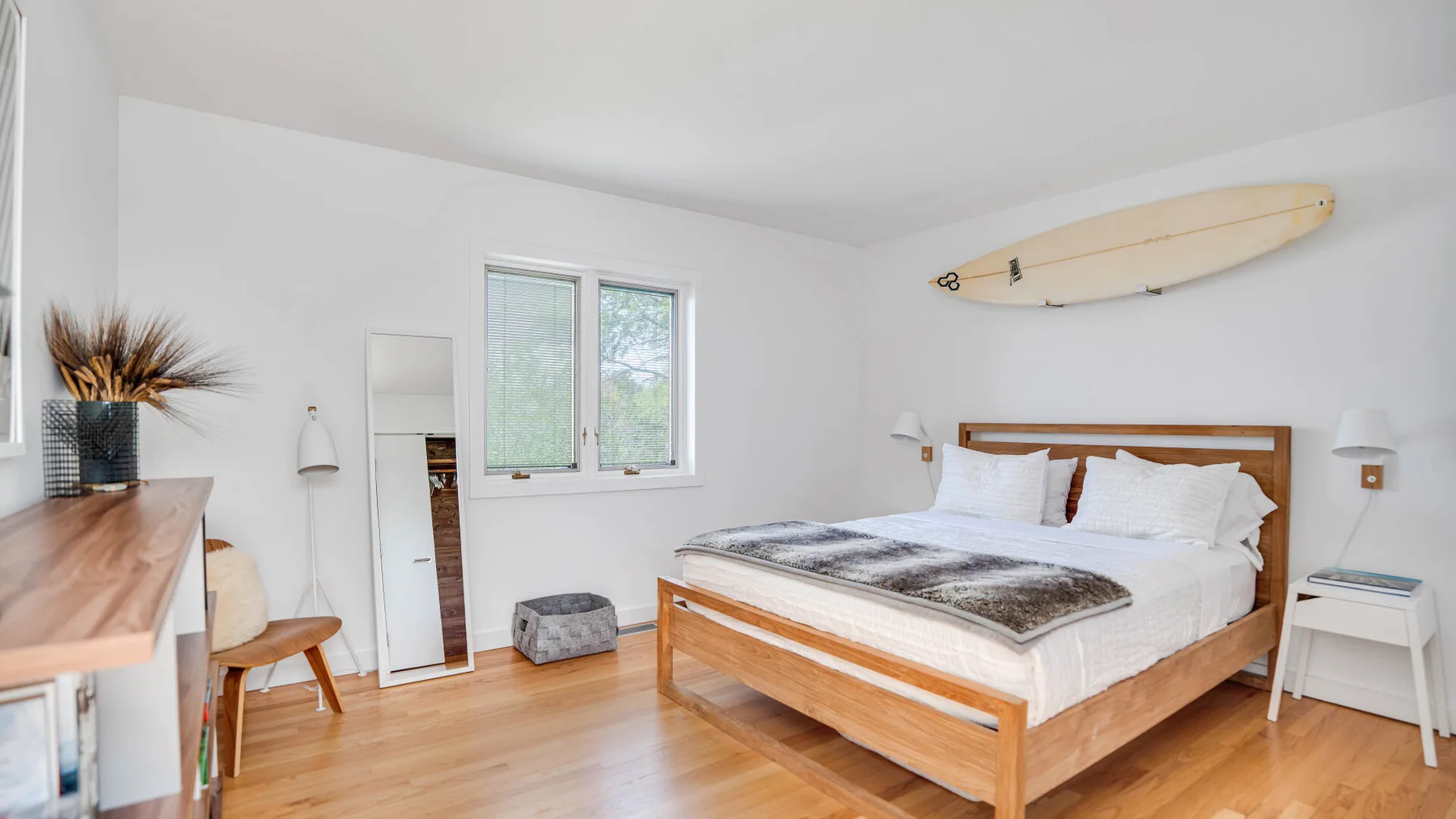 A bright bedroom with a wooden bed and a surfboard mounted above it.