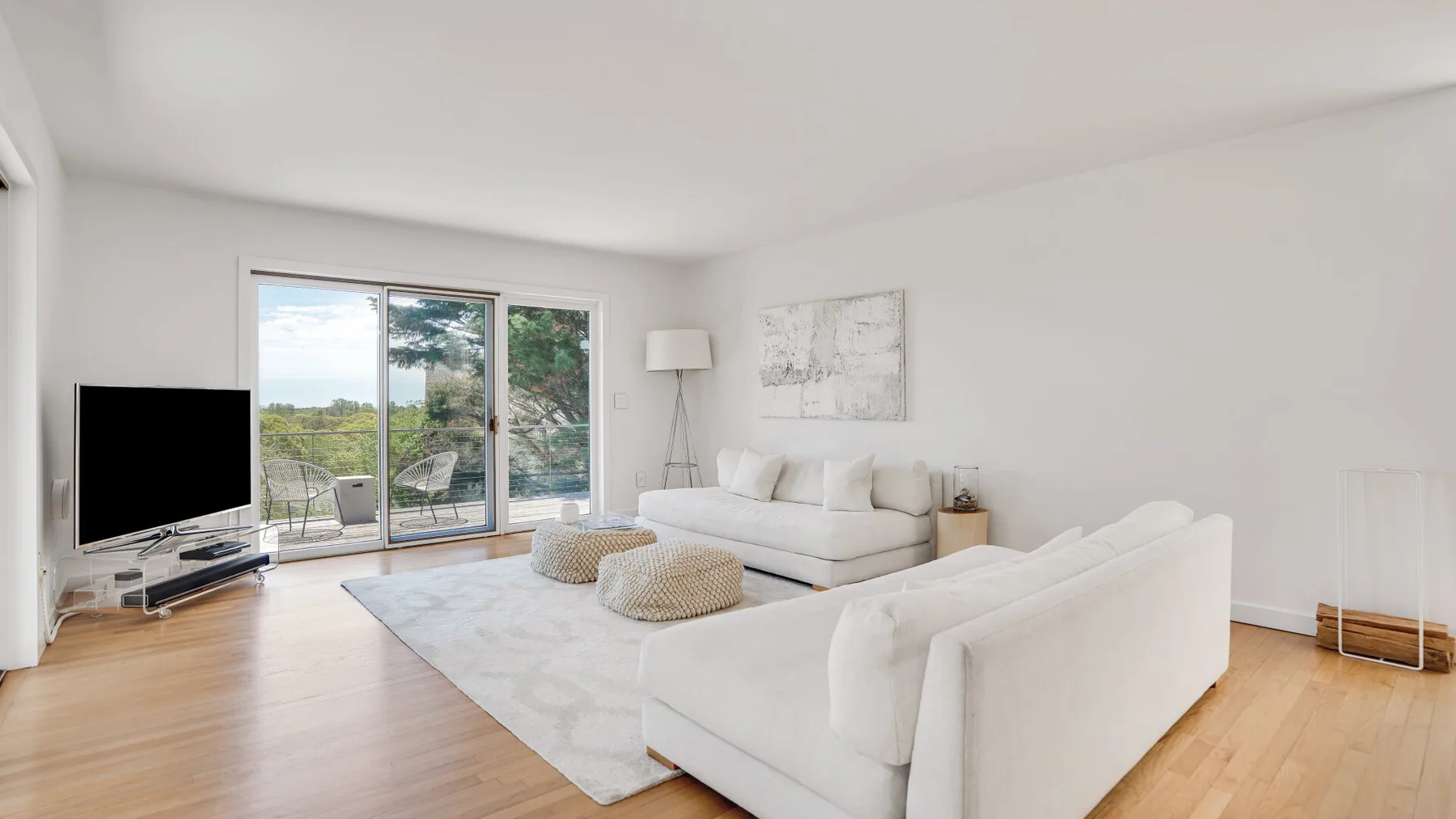 A bright living room with white seating and large glass doors opening to a green view.