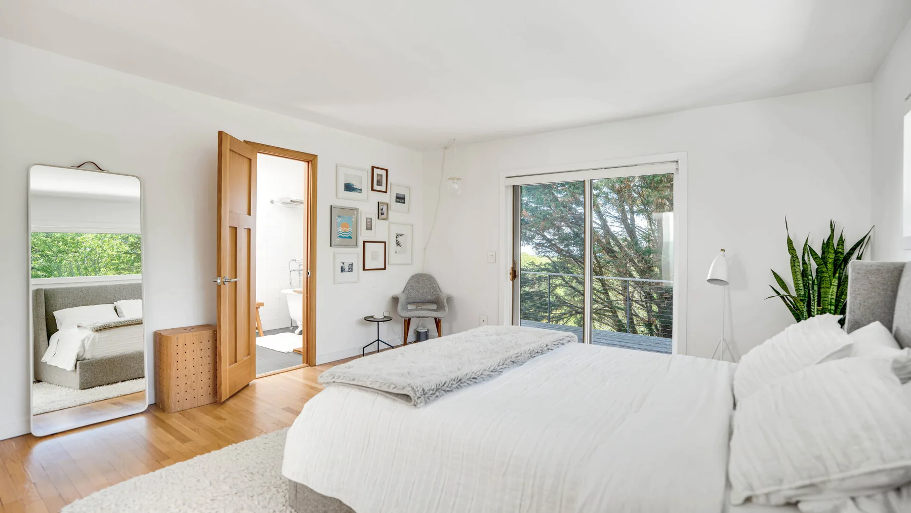 A bright bedroom with a large bed and sliding glass doors opening to a leafy view.